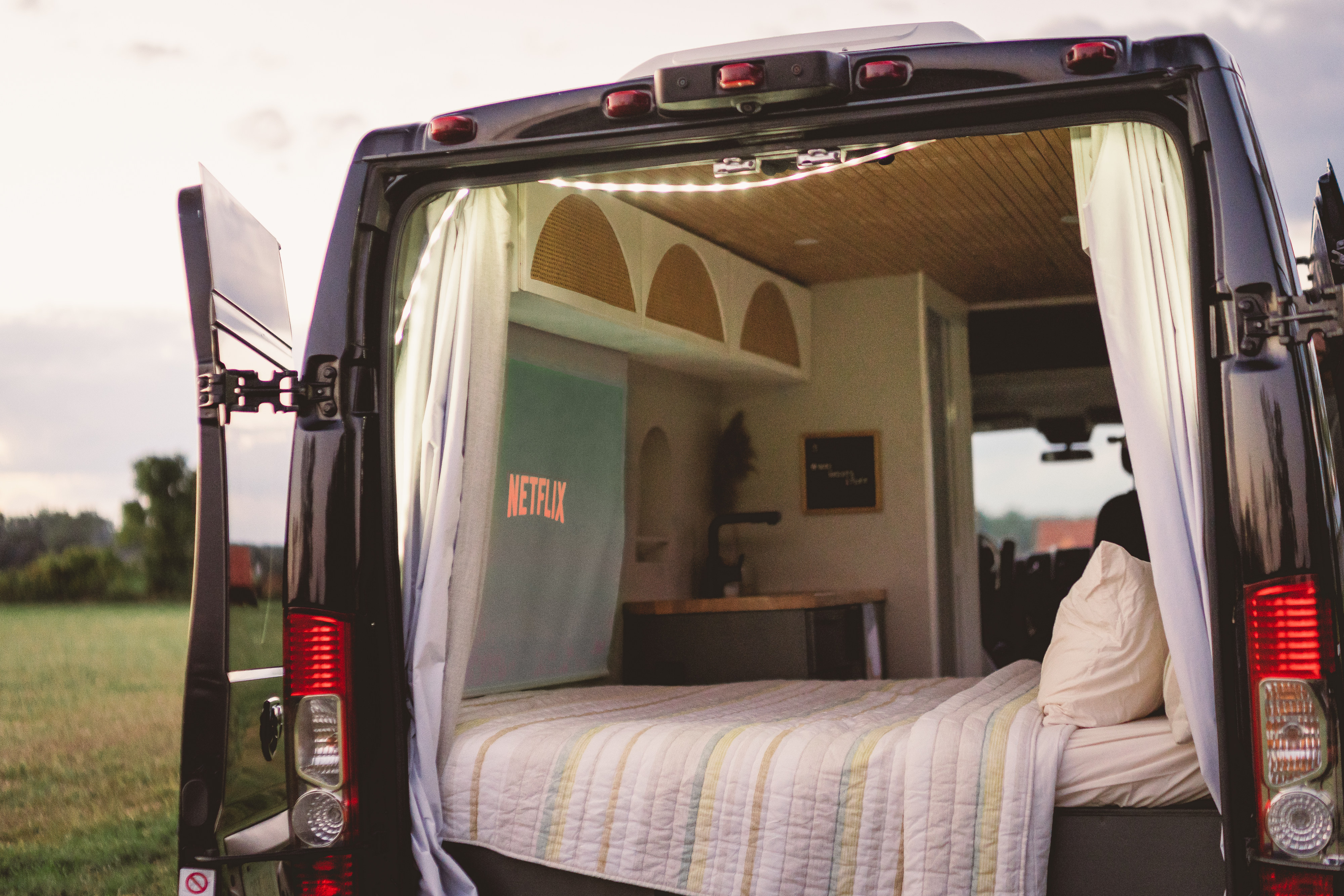 Enjoy cozy comfort in this rv rental. Rear view shows a bed, Netflix projection, and kitchen. Perfect for van life adventures.. Other Other 2015