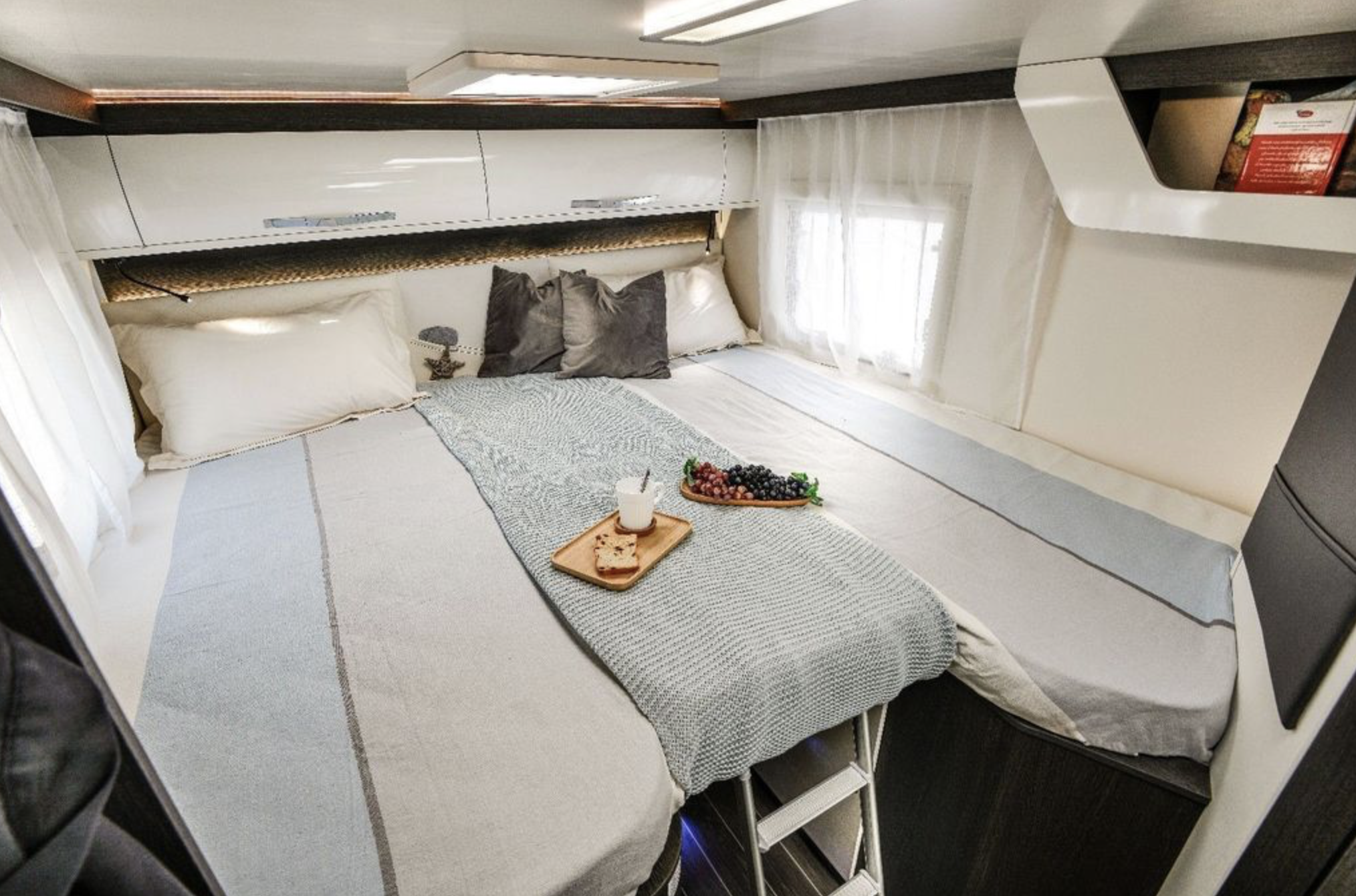 Bright RV rental bedroom: large bed with a breakfast tray, sleek overhead cabinets, and soft natural light.. Roller Team 685 Zefiro 2022