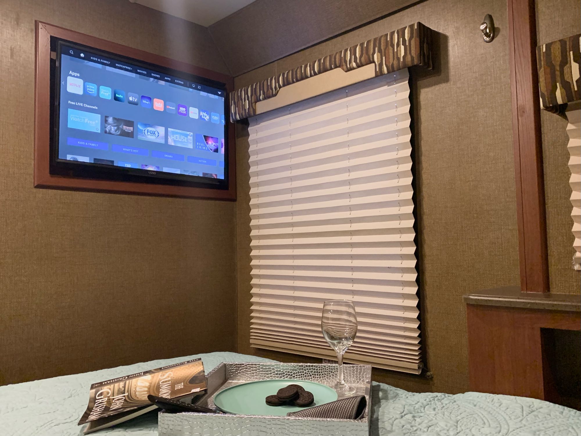 Cozy RV rental bedroom featuring wall-mounted TV, window blind, and a bed tray with cookies & a book. Relaxing travel.. Thor Vegas 2016