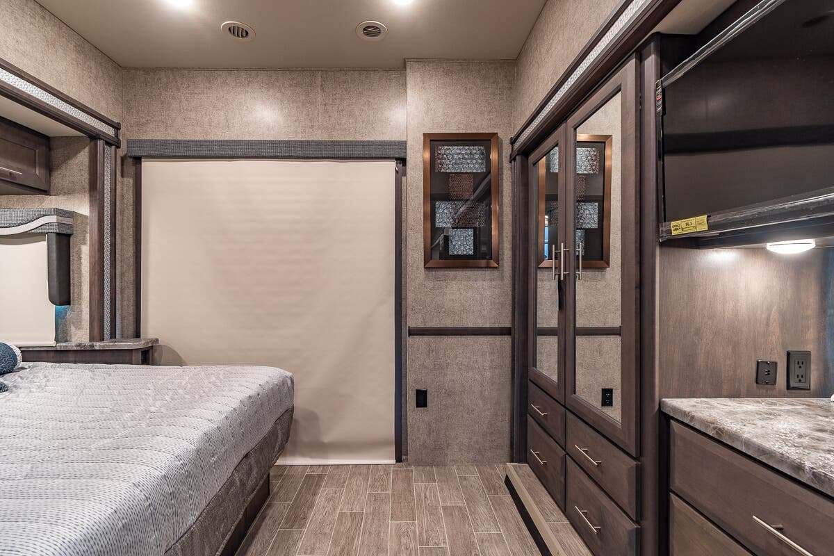 RV rental bedroom interior with a comfortable bed, mirrored wardrobe, and TV mounted above a counter.. Thor Motor Coach Outlaw 2022