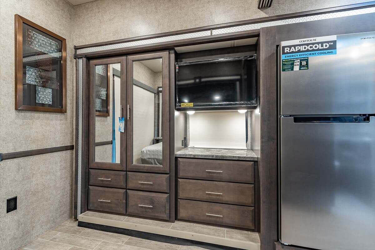 Inside an RV rental: dark wood storage with mirrored doors, TV, and a large stainless steel refrigerator for comfortable living.. Thor Motor Coach Outlaw 2022