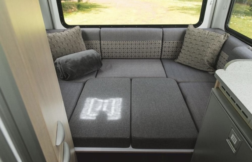 Cozy RV rental interior: grey modular seating converts to a bed, with pillows & blanket. Features a compact kitchenette.. LDV Kea Breeze 2016