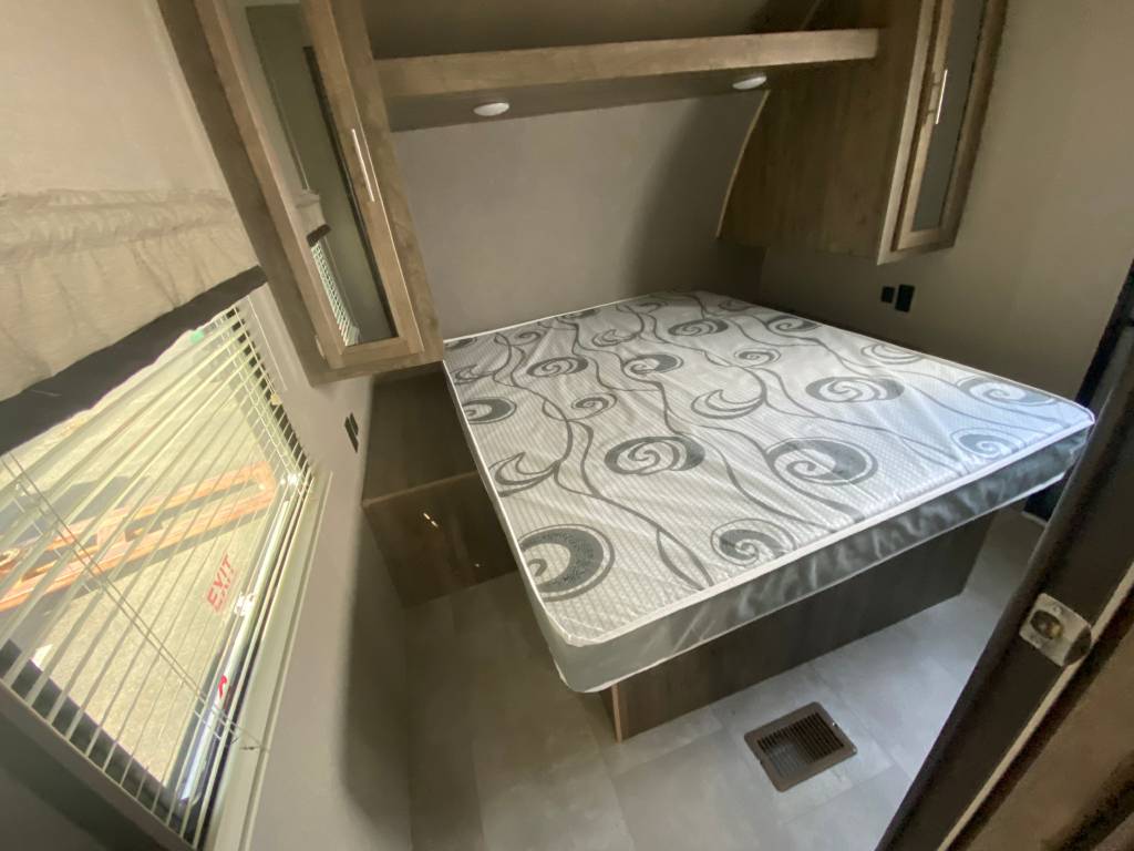 Spacious RV rental bedroom featuring a comfortable patterned mattress, overhead cabinets, and a large window with blinds.. Coachmen Other 2021
