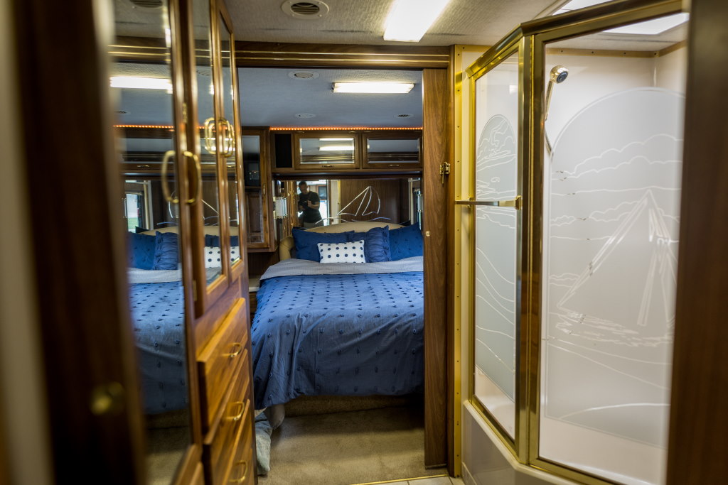 Inside an RV rental: a comfortable bedroom with blue bedding and a unique shower with sailboat-etched glass. Ideal for adventures.. National RV Tradewinds 2000