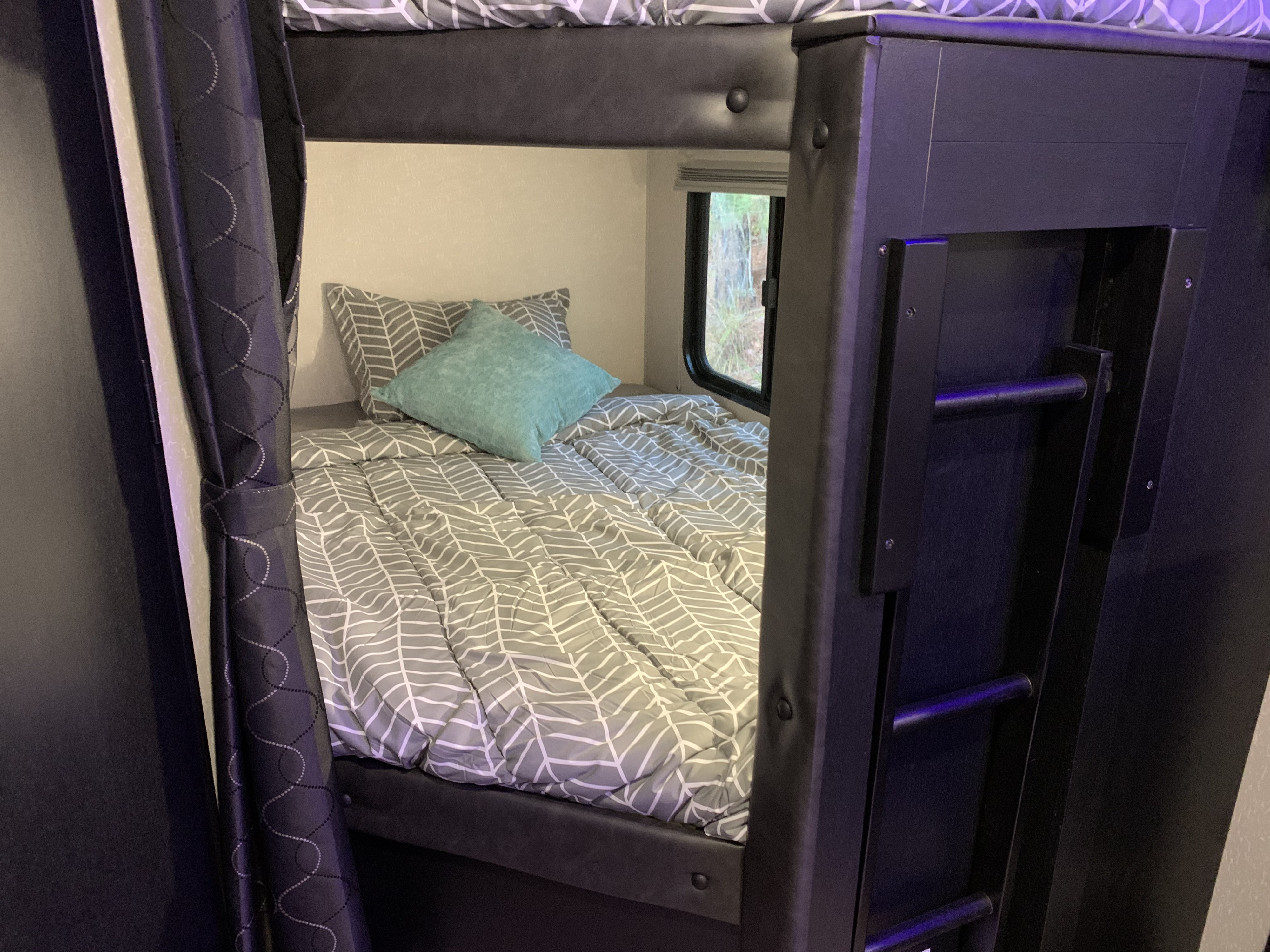 Cozy bunk bed setup in an RV rental, with gray patterned bedding and a side window, perfect for trips.. Forest River Cherokee Grey Wolf 2022