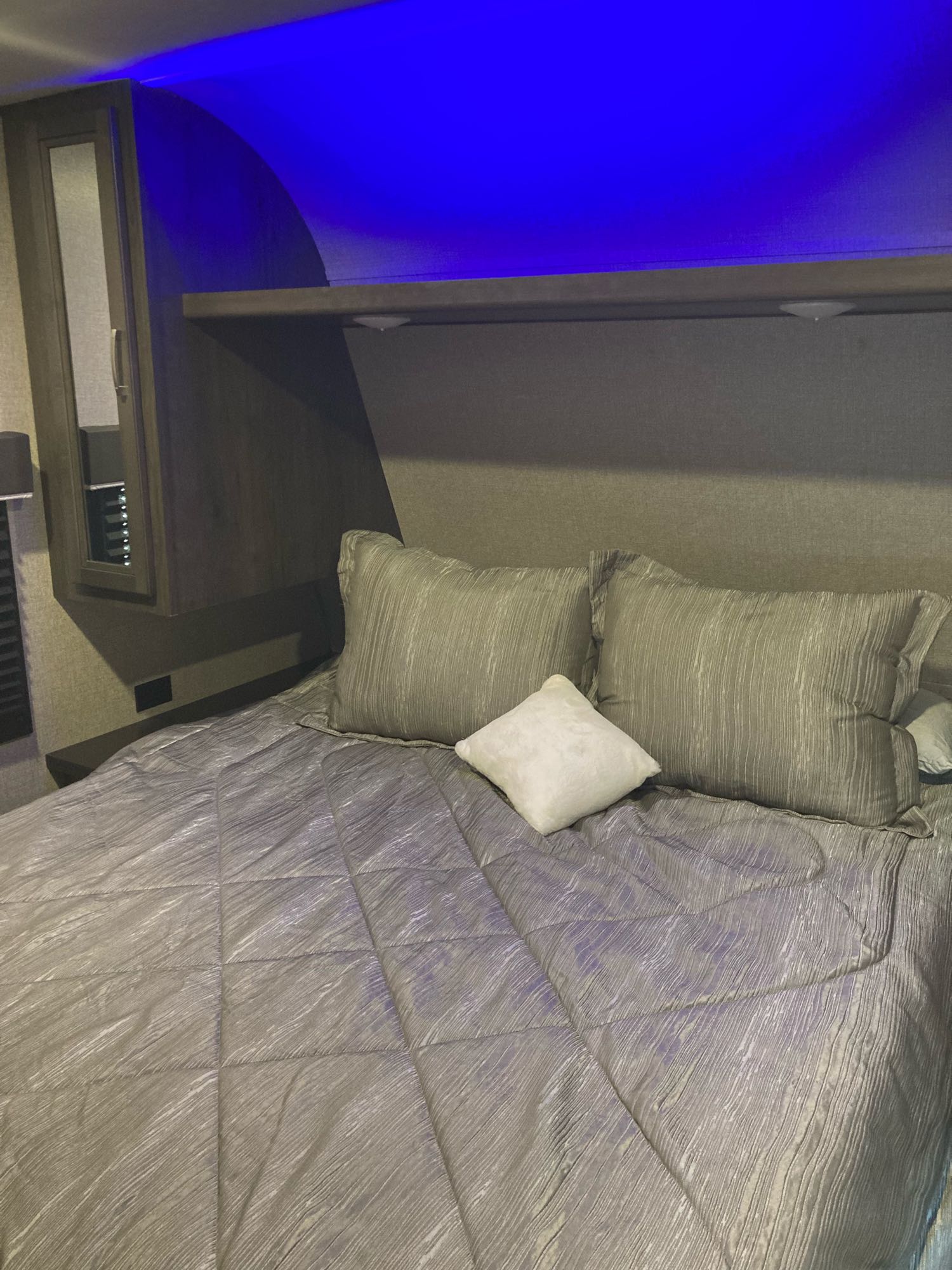 RV rental's inviting bedroom: A cozy grey bed with pillows beneath modern blue LED strip lighting and overhead storage.. Jayco Jay Flight SLX Baja Edition 2020