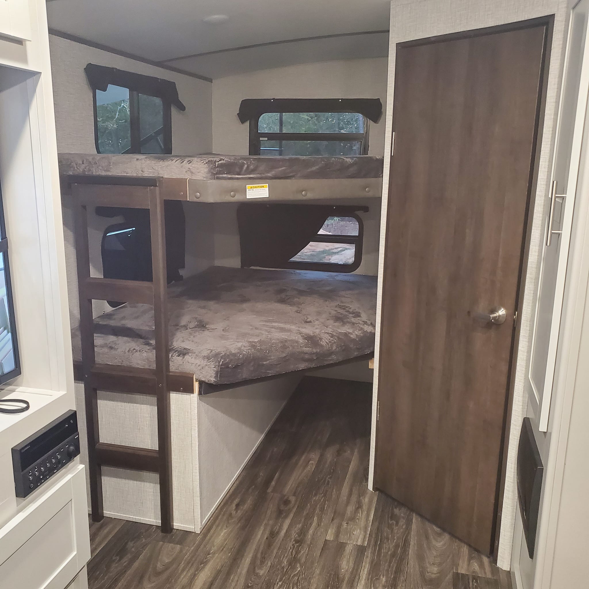 Interior view of an RV rental showing modern bunk beds with windows, a ladder, and sleek wood-look flooring.. Keystone RV Bullet Premier Ultra 2021
