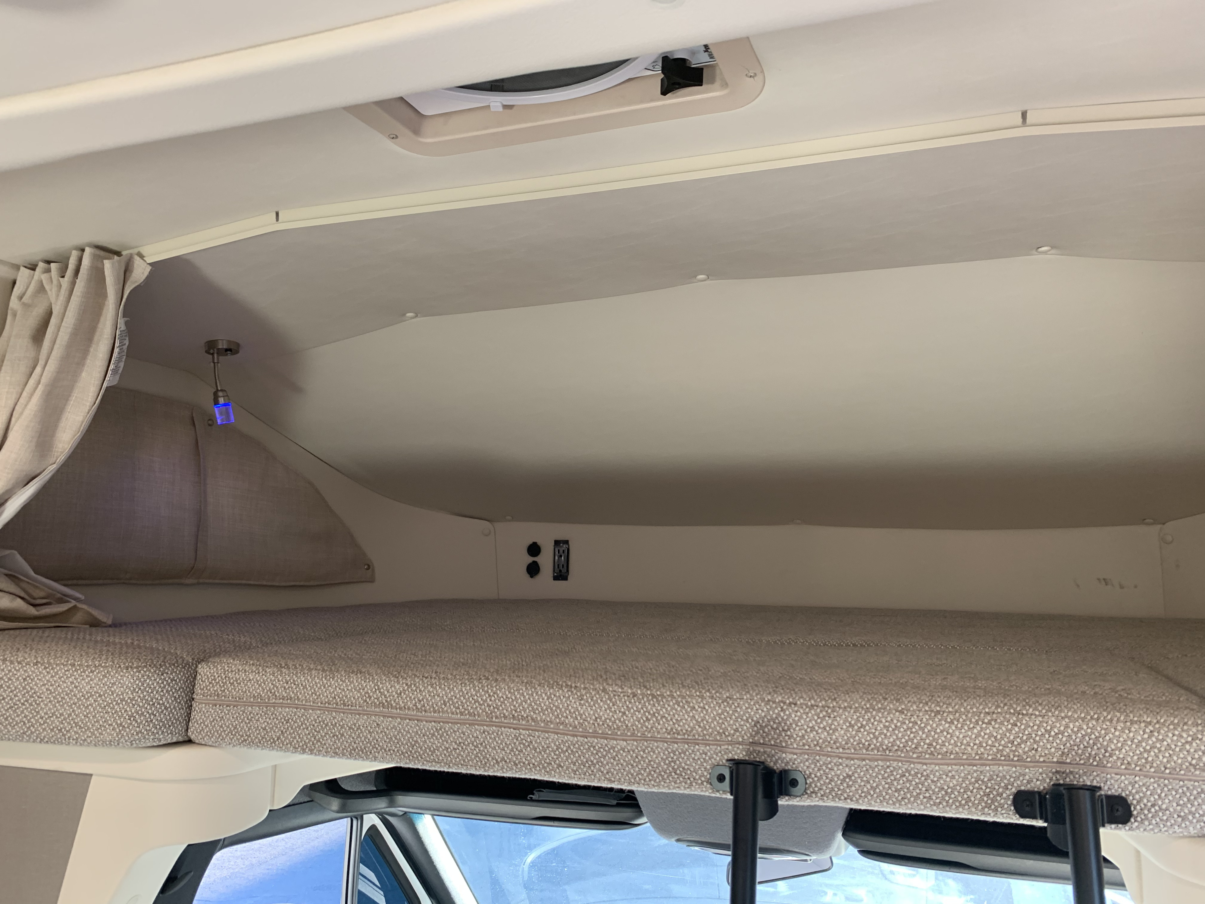 Cozy RV rental overhead bunk bed with curtains, ceiling vent, and power outlets for comfortable sleeping.. Winnebago View 2020