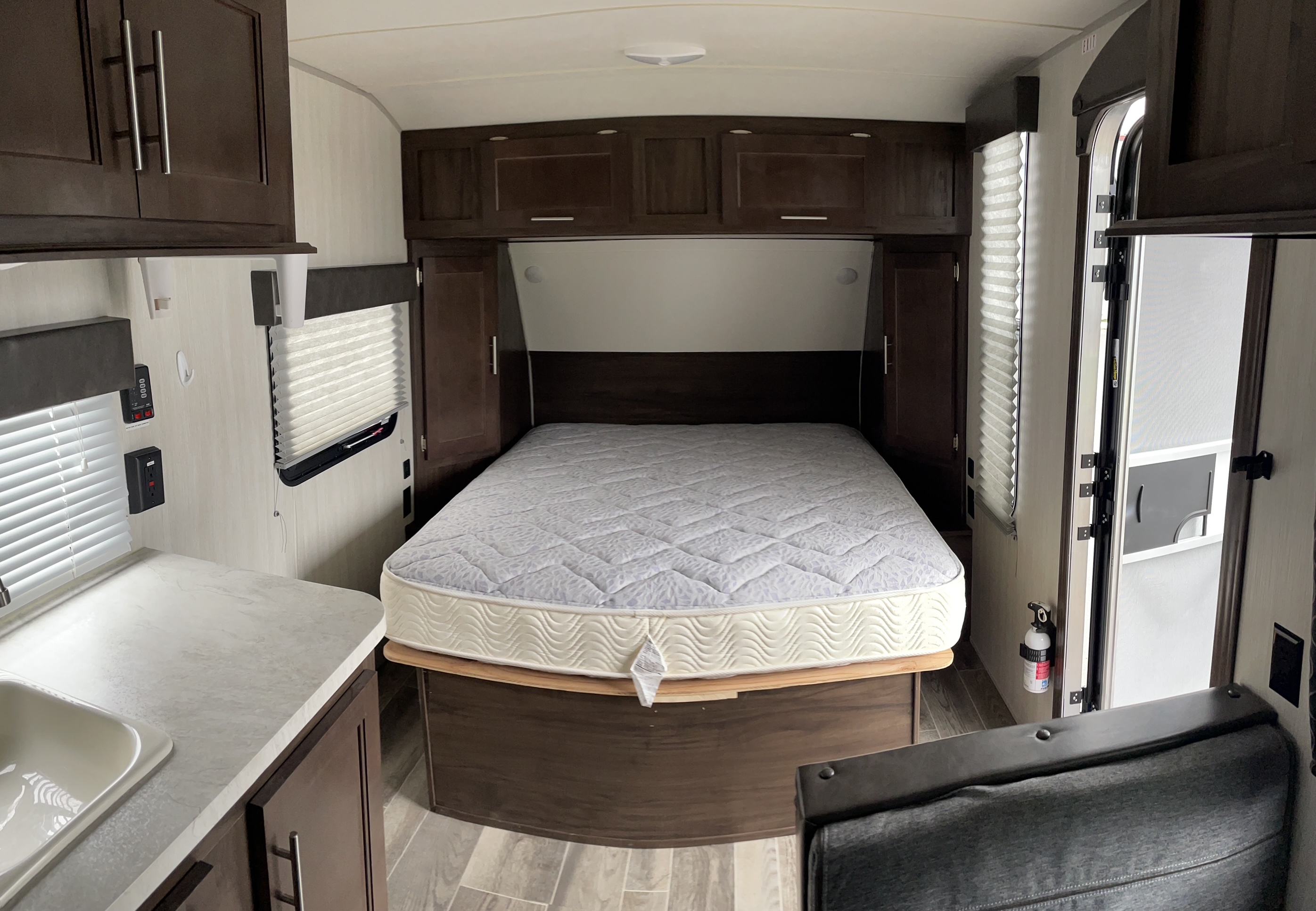 Inside an RV rental: a cozy bedroom with a queen mattress, dark wood cabinets, and a glimpse of the kitchen sink and living area.. Forest River Cherokee Wolf Pup 2019