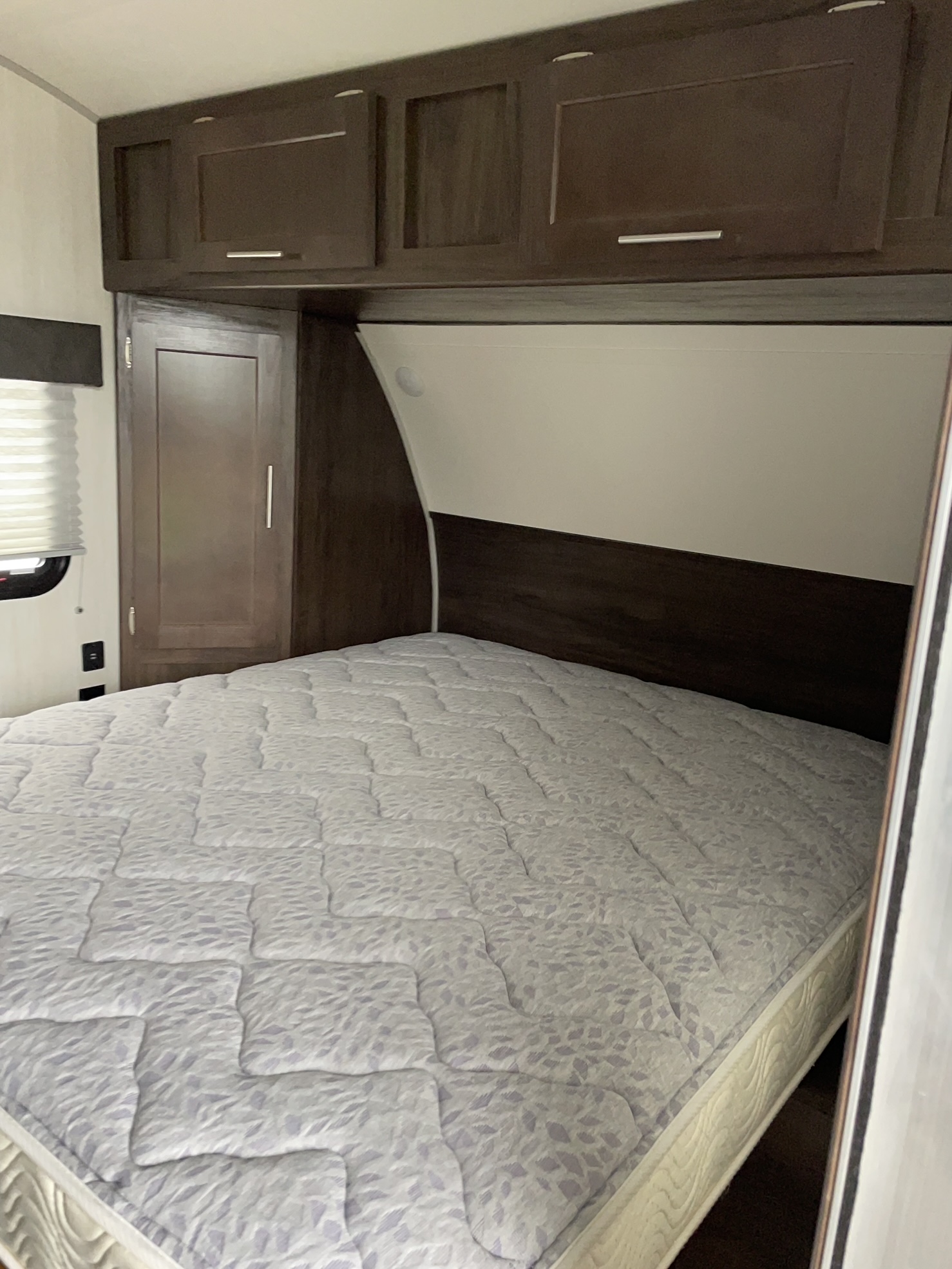Cozy RV rental bedroom features a comfortable bed, wood-toned headboard, overhead cabinets, and a convenient wardrobe.. Forest River Cherokee Wolf Pup 2019
