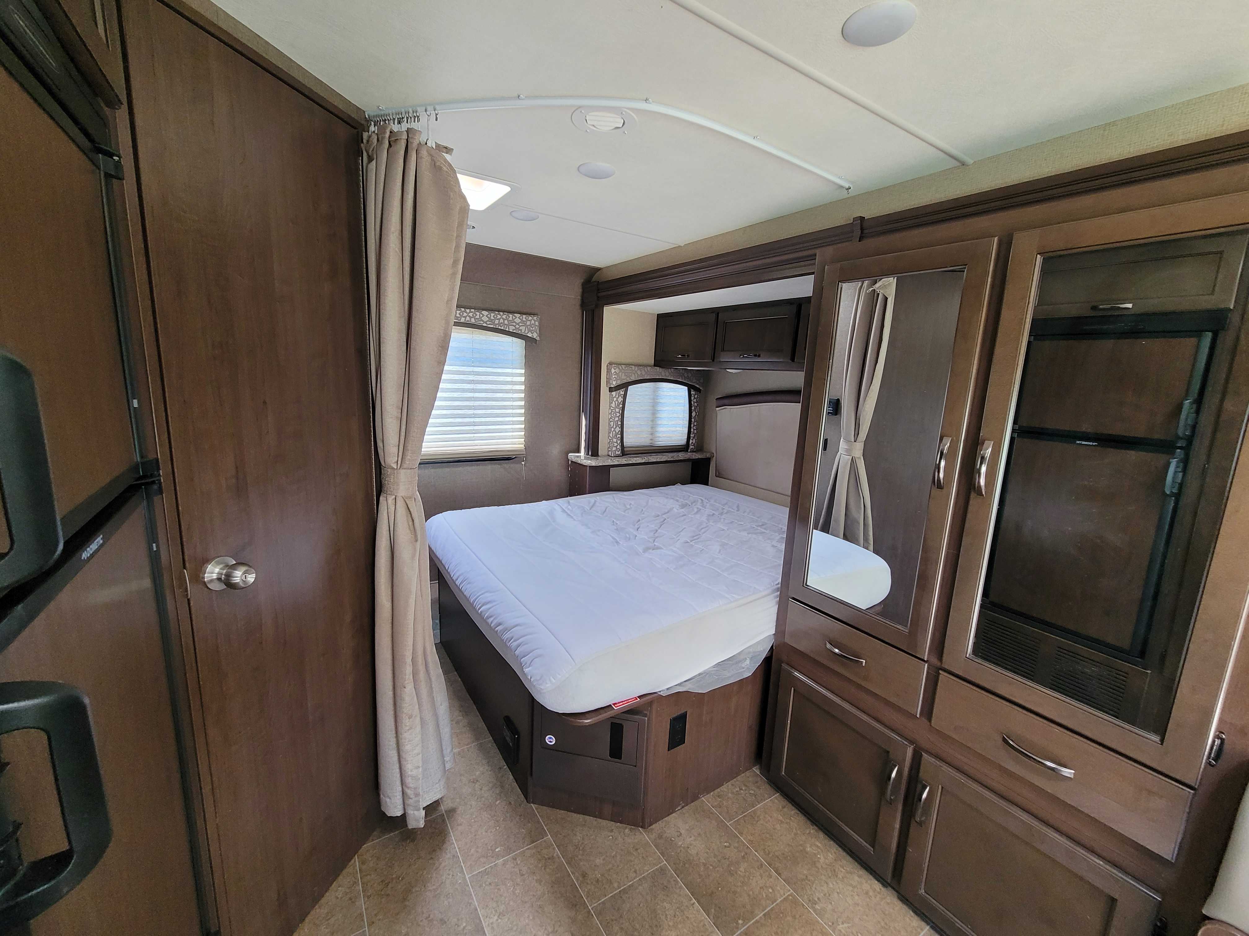 Spacious rv rental bedroom featuring a comfy bed, rich wood cabinetry, convenient storage, and natural light.. Thor Chateau 2018