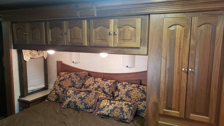 Cozy RV rental bedroom showing a comfortable bed, overhead wooden cabinets with lighting, and a built-in wardrobe.. Allegro Allegro Bus 2005