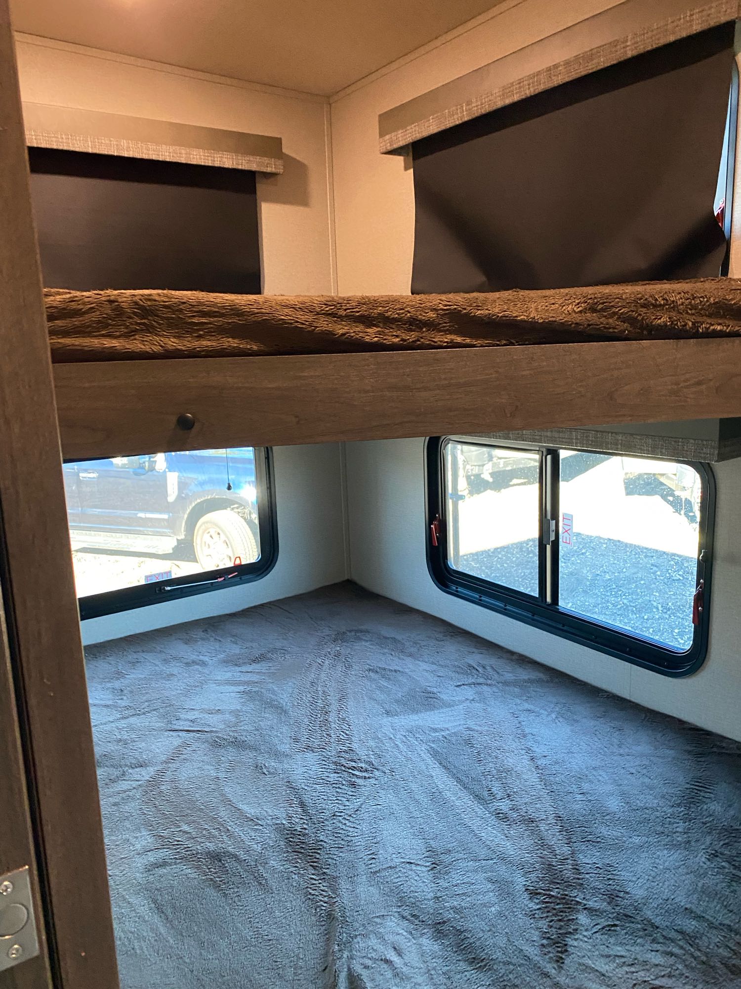 Inside an RV rental: Two bunk beds with windows; top has a dark shade, bottom shows a truck outside.. Grand Design Solitude 2021