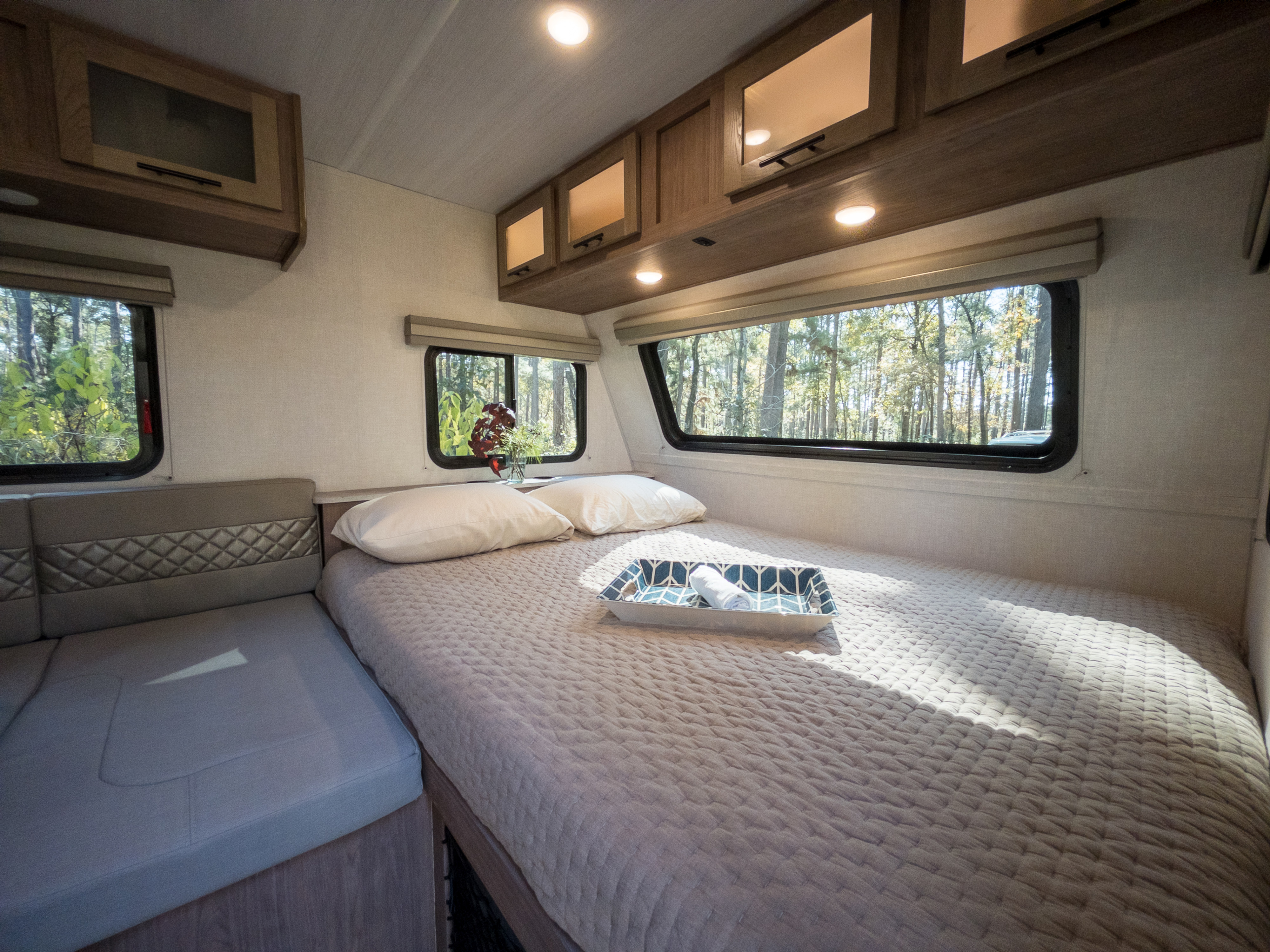 Cozy RV rental bedroom with a comfortable bed, convenient storage, and large windows offering a beautiful forest view.. Forest River NOBO 19.7 2022