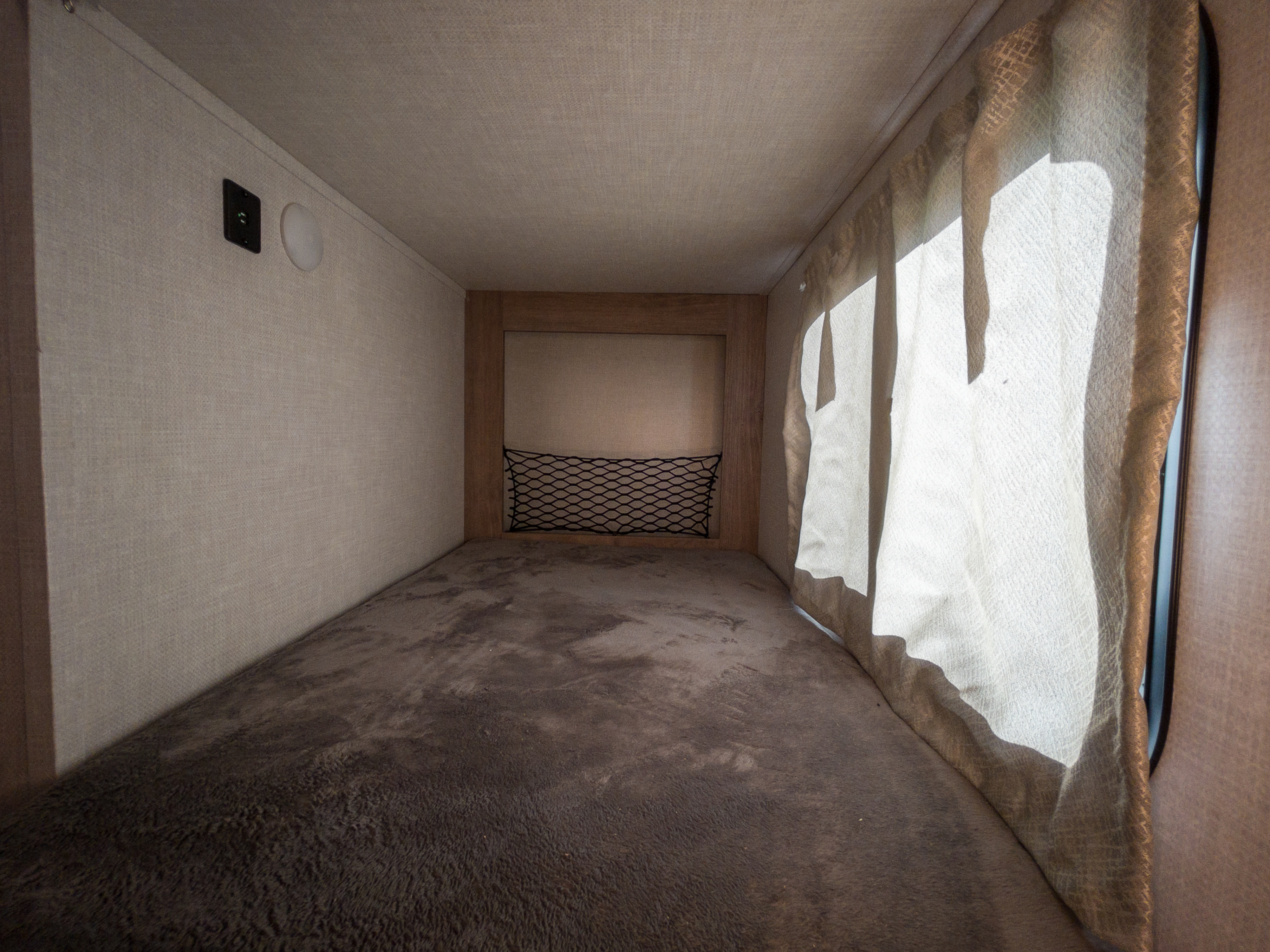 Inside an RV rental: a carpeted bunk bed with a charging port, light, and curtained window, offering a compact sleeping space.. Forest River NOBO 19.7 2022