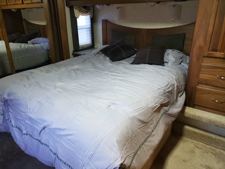 Cozy RV rental bedroom showing a large bed, wooden headboard, and built-in storage. Note the steps for easy access.. Allegro Allegro Bus 2005