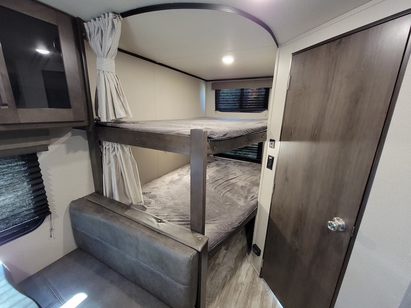 This RV rental features a modern bunk bed setup with privacy curtains, a cabinet, and a door for a family-friendly camping experience.. Other Other 2021