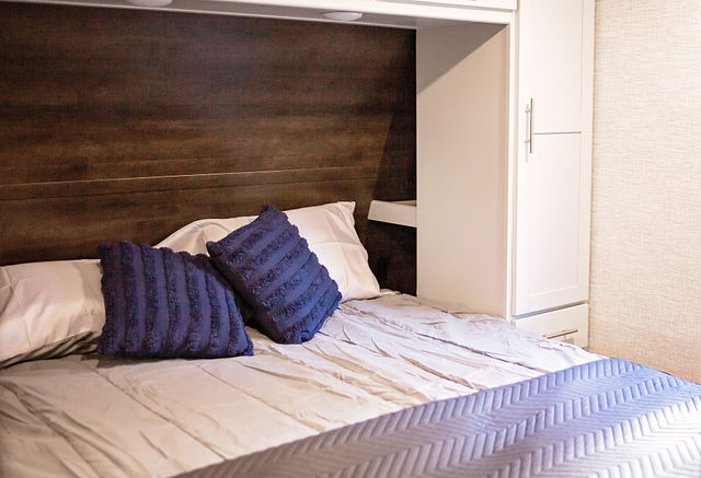 RV rental bedroom featuring a comfortable bed with navy pillows, light bedding, and a dark wood headboard.. Keystone RV Bullet Premier Ultra 2021