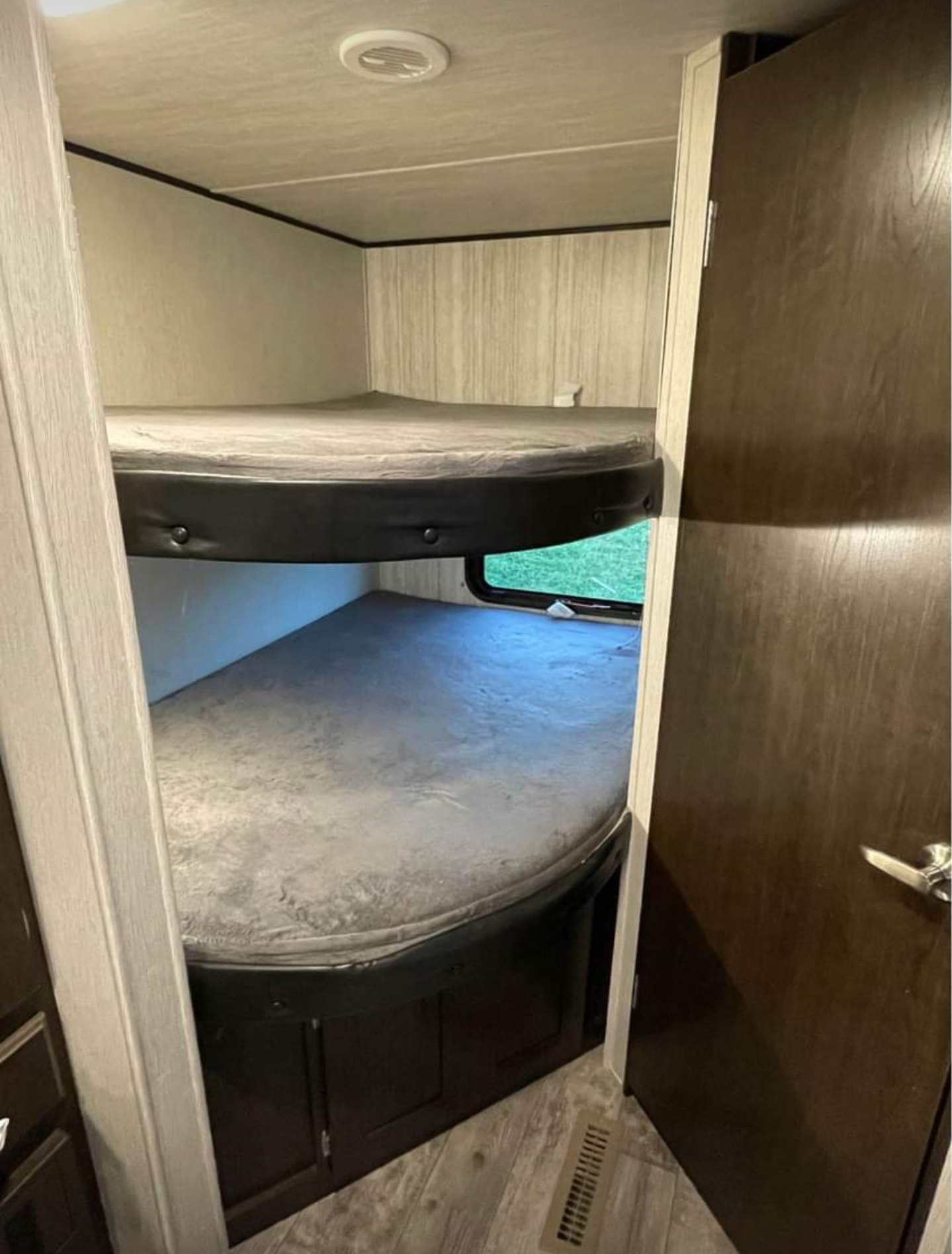 An RV rental's bunk bed area: two grey beds, lower cabinets, and a window. Compact & functional sleeping space.. Heartland RVs Pioneer 2019