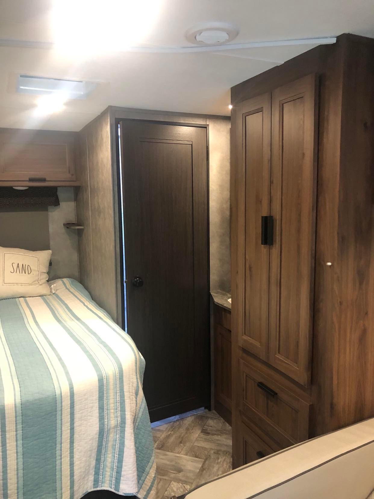 Cozy RV rental bedroom with blue striped bed, dark door, and wood cabinets. Compact and functional travel space.. Forest River Other 2021