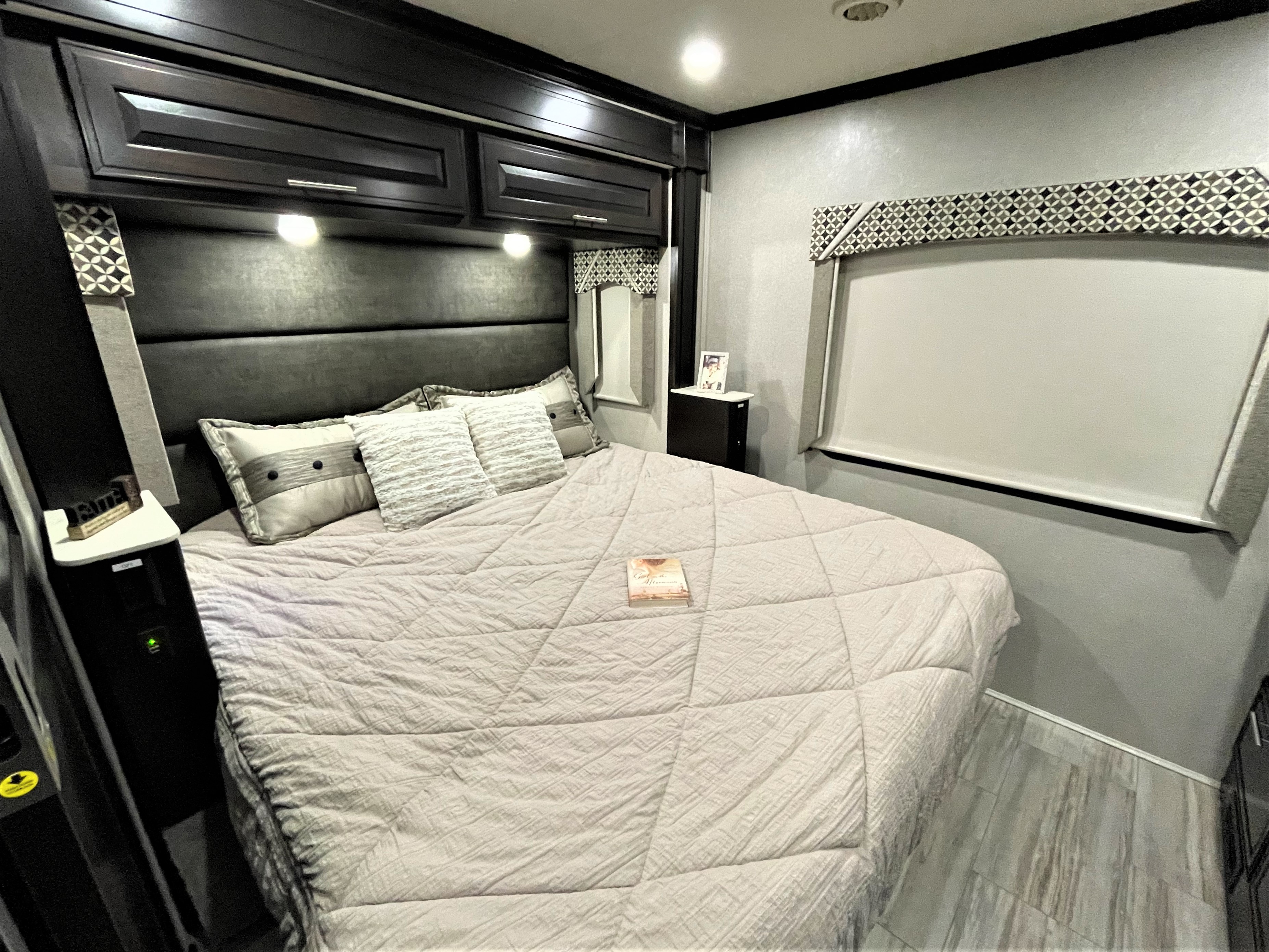 Spacious RV rental bedroom featuring a large bed with neutral bedding, dark wood overhead cabinets, and bedside tables.. Dynamax Corp Dx3 2020