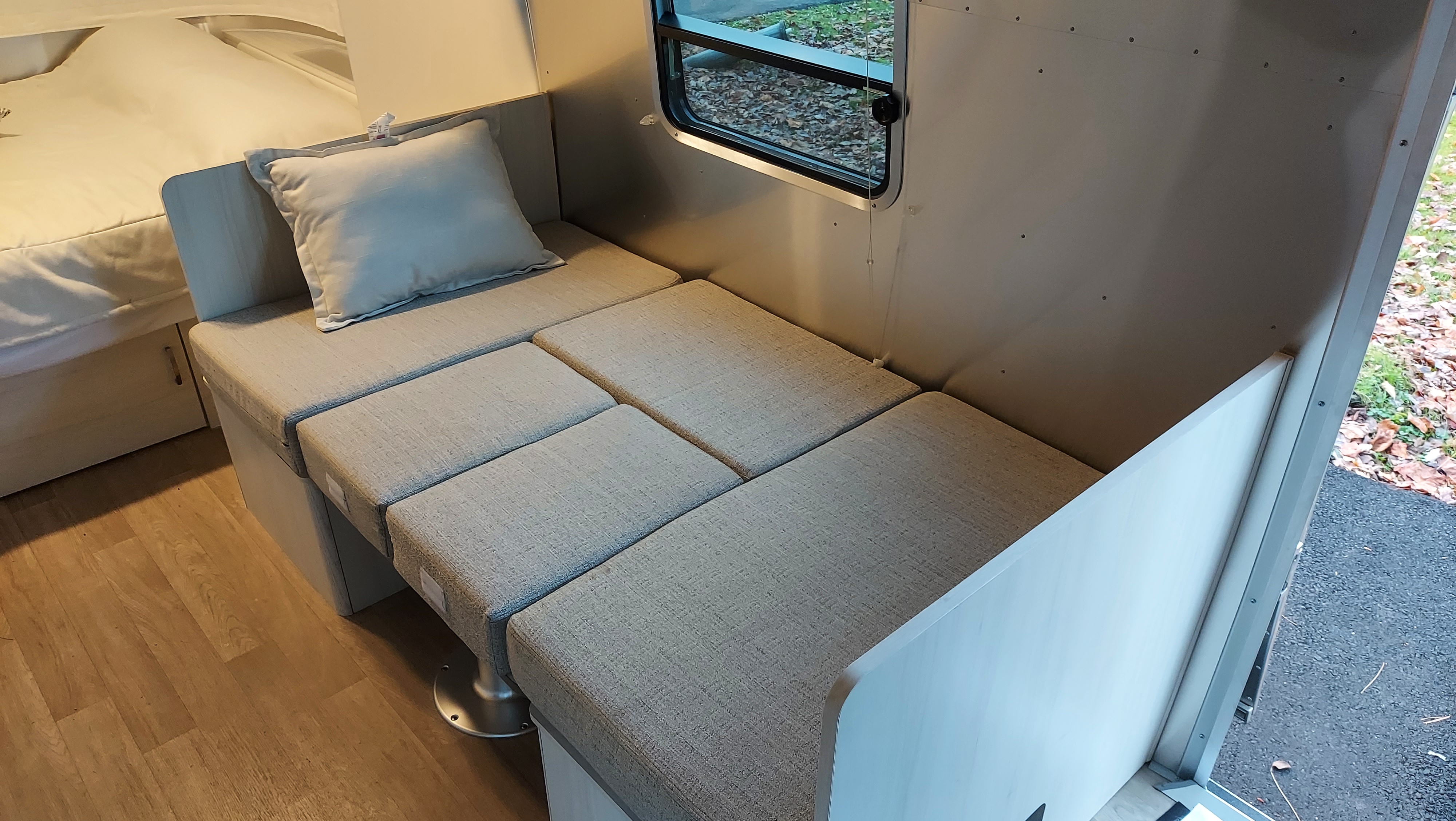 Comfortable RV rental interior: Light-colored cushions, a compact window, and a flexible seating/bed area.. Airstream Bambi 2021