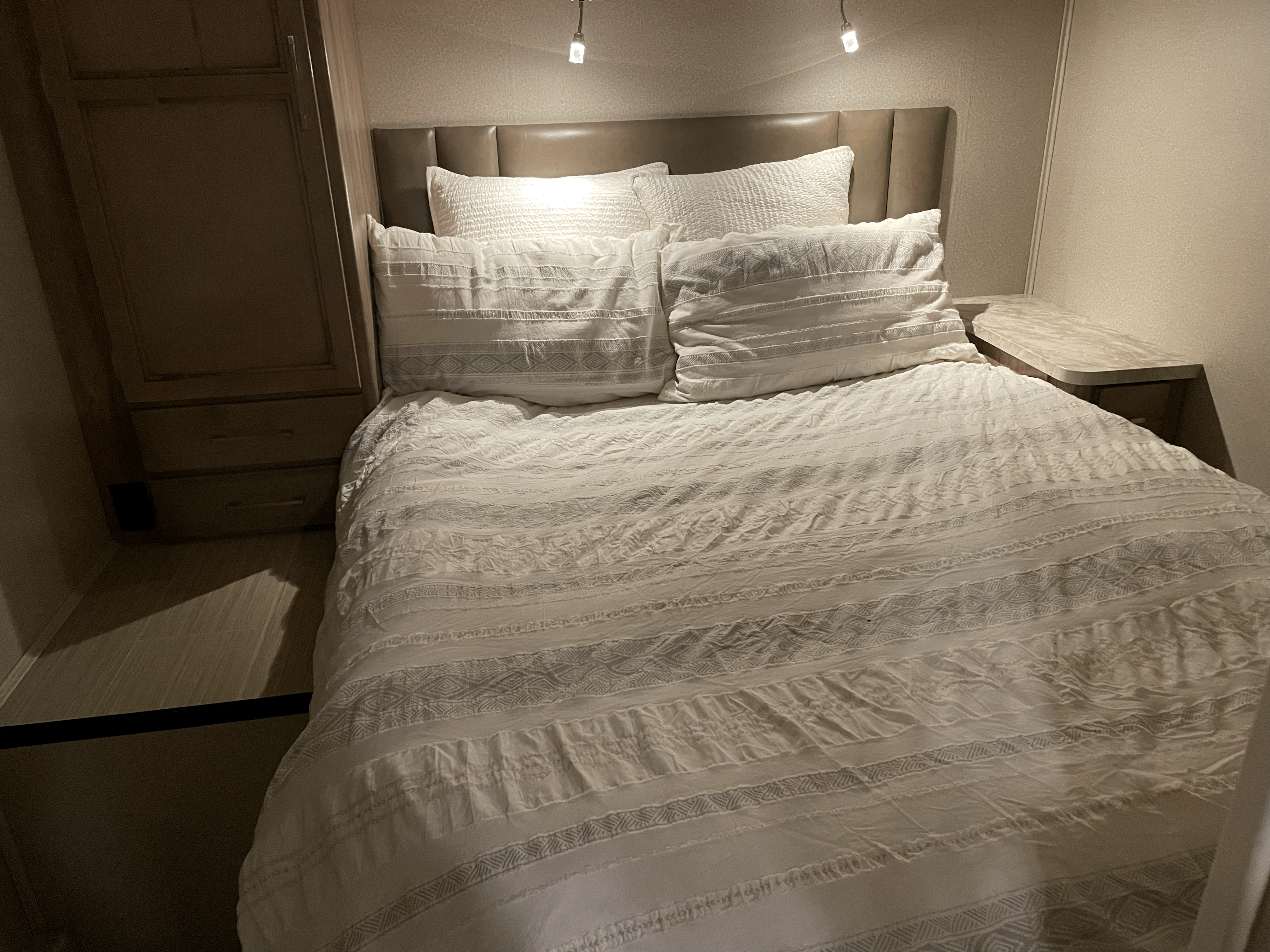 Cozy RV rental bedroom featuring crisp white bedding, a padded headboard, built-in storage, and task lighting.. Entegra Coach Odyssey 2020