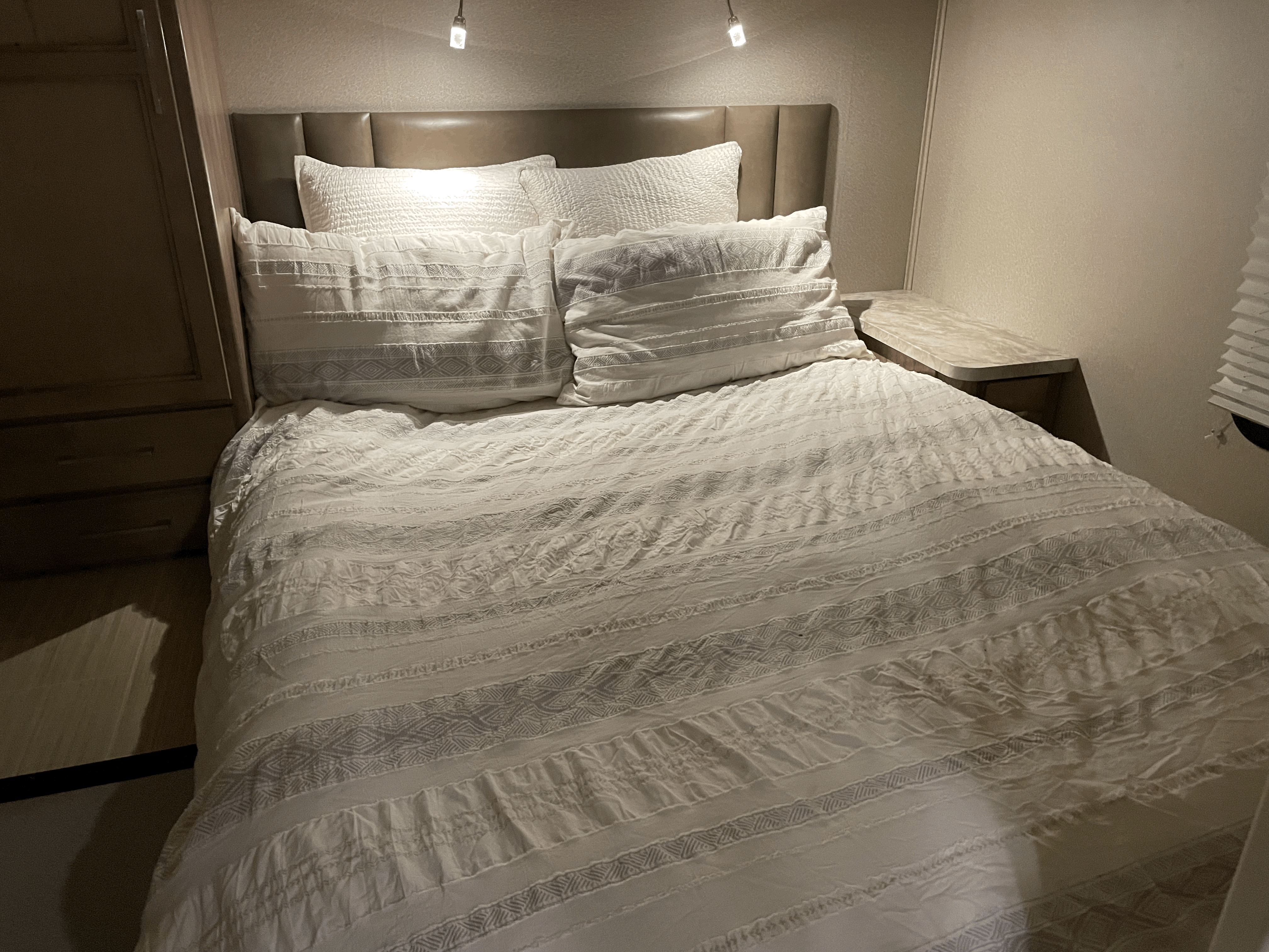 Cozy RV rental bedroom featuring a comfortable bed with white textured bedding, headboard, and built-in storage.. Entegra Coach Odyssey 2020