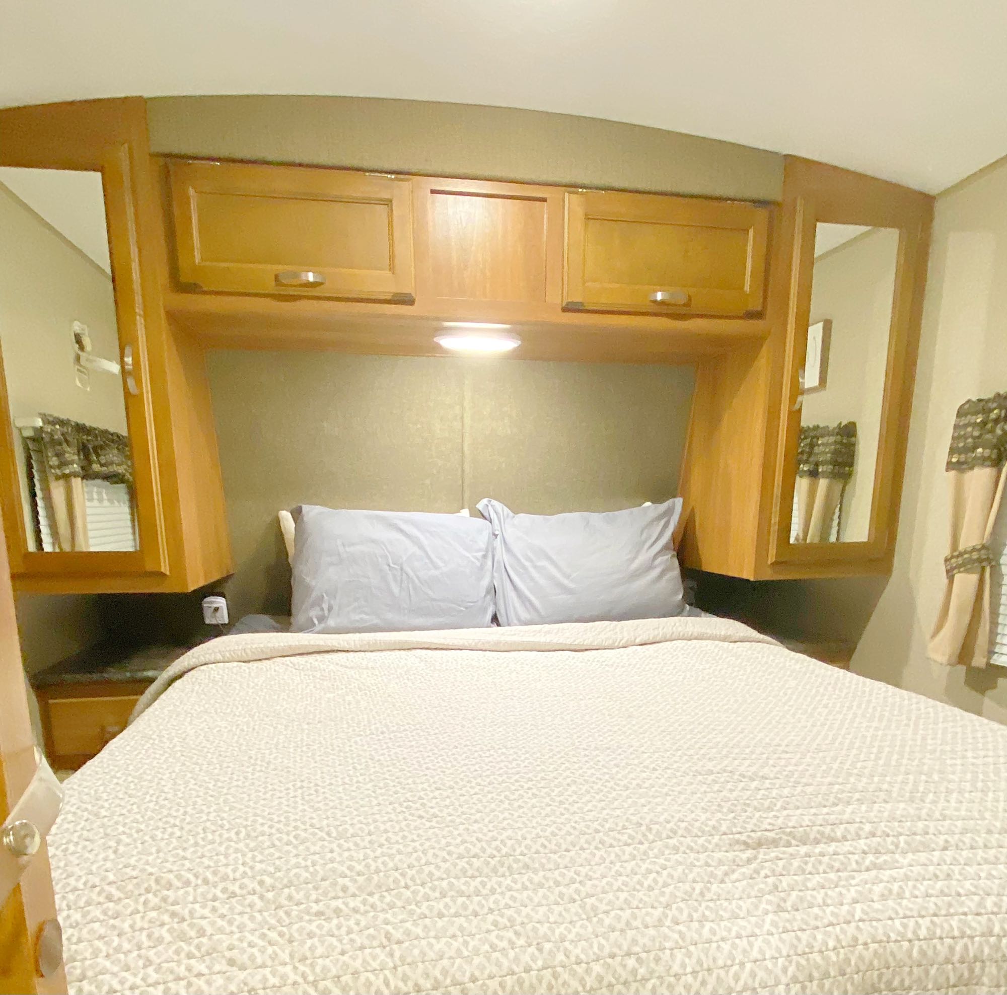 Cozy RV rental bedroom featuring a full bed, overhead storage cabinets, and mirrored wardrobes. Perfect for travel.. keystone Springdale 2017