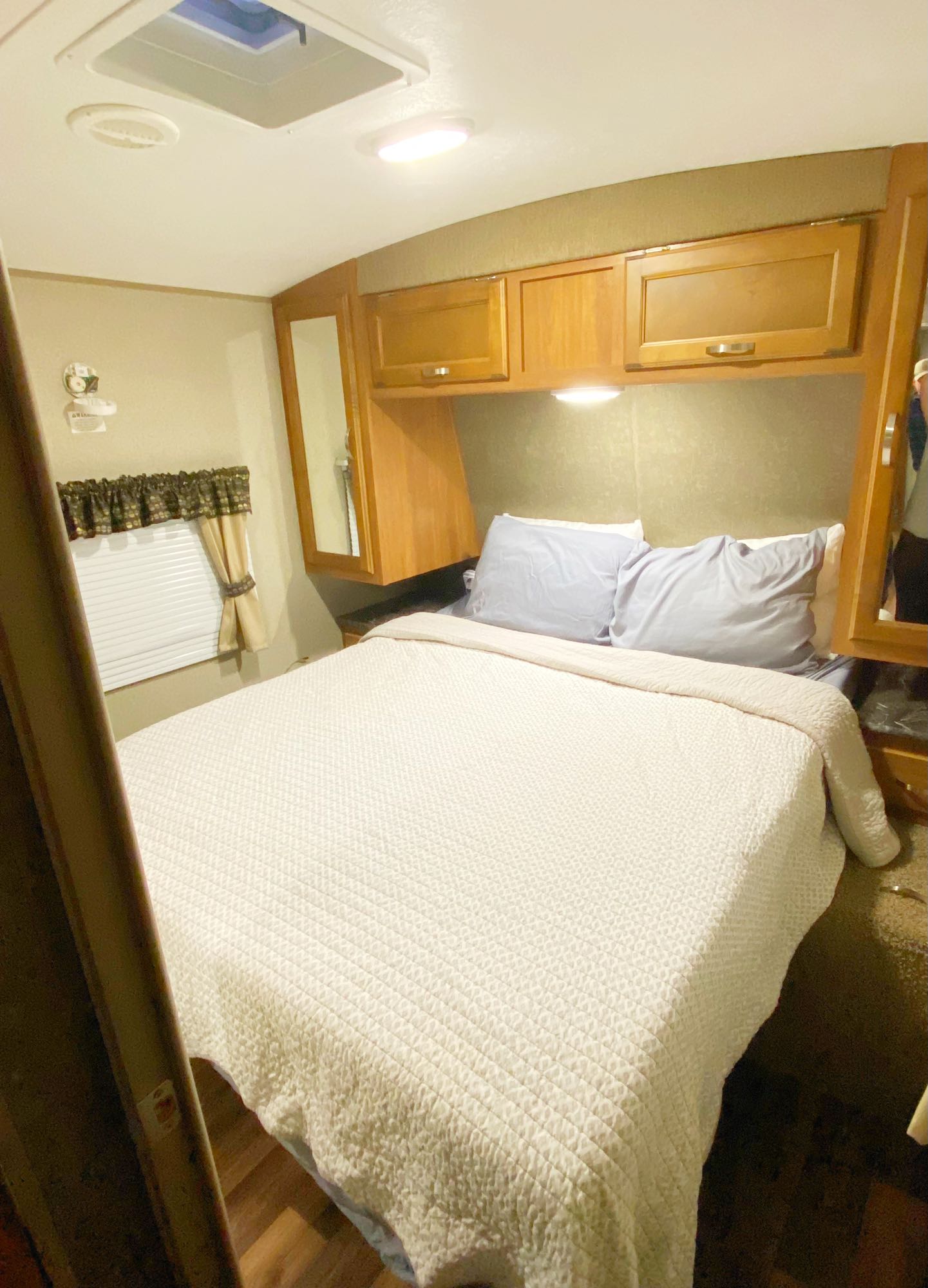 A queen bed fills this clean RV rental bedroom, featuring overhead storage, a window with blinds, and bright lighting.. keystone Springdale 2017