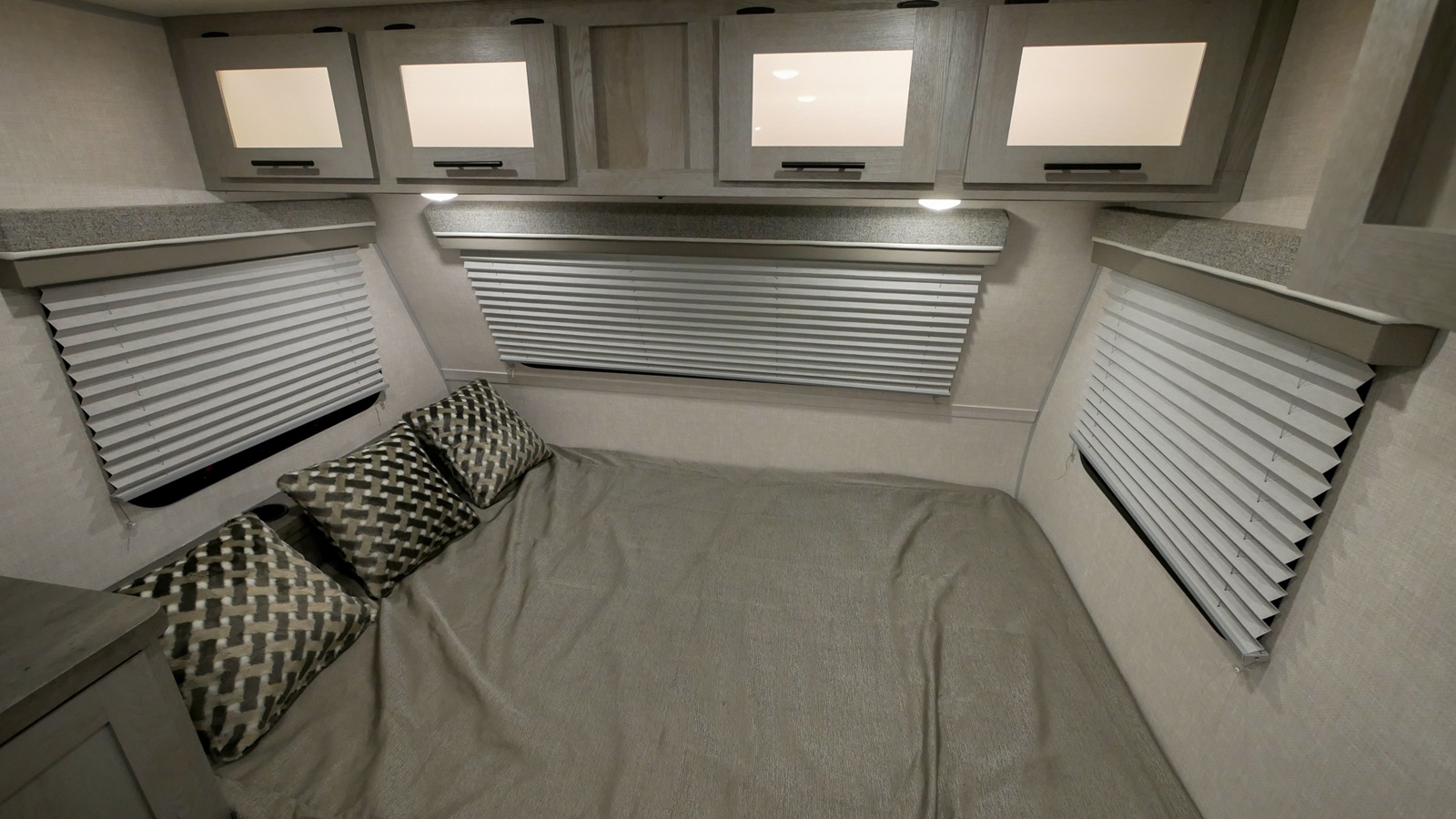 RV rental bedroom. Features a comfy bed with patterned pillows, pleated window blinds, and overhead cabinets for storage.. Forest River Ibex 2021