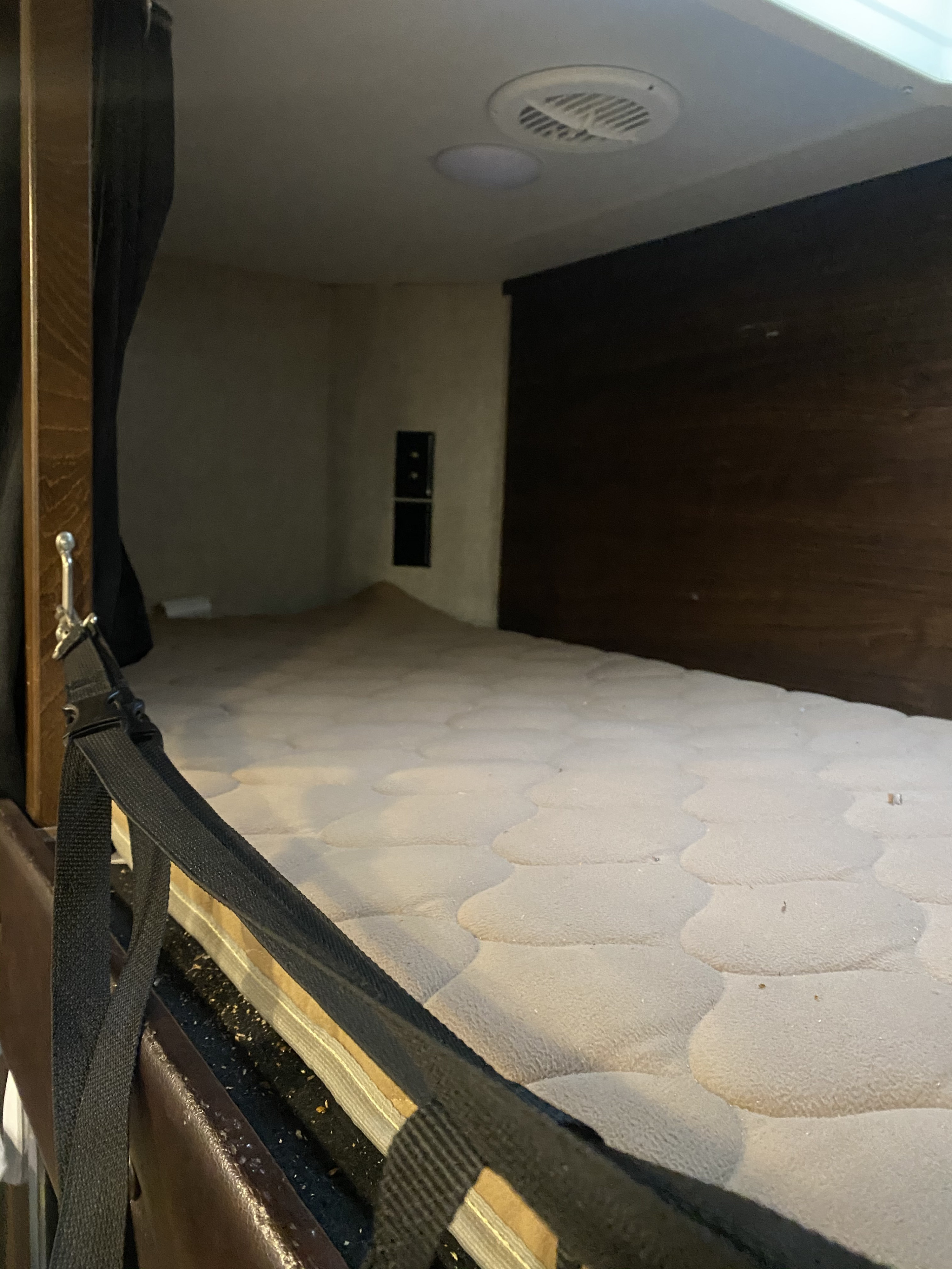 RV rental bunk bed interior, showing a cozy sleeping area with a quilted mattress, safety strap, and ceiling fixtures.. Heartland Cyclone 2015