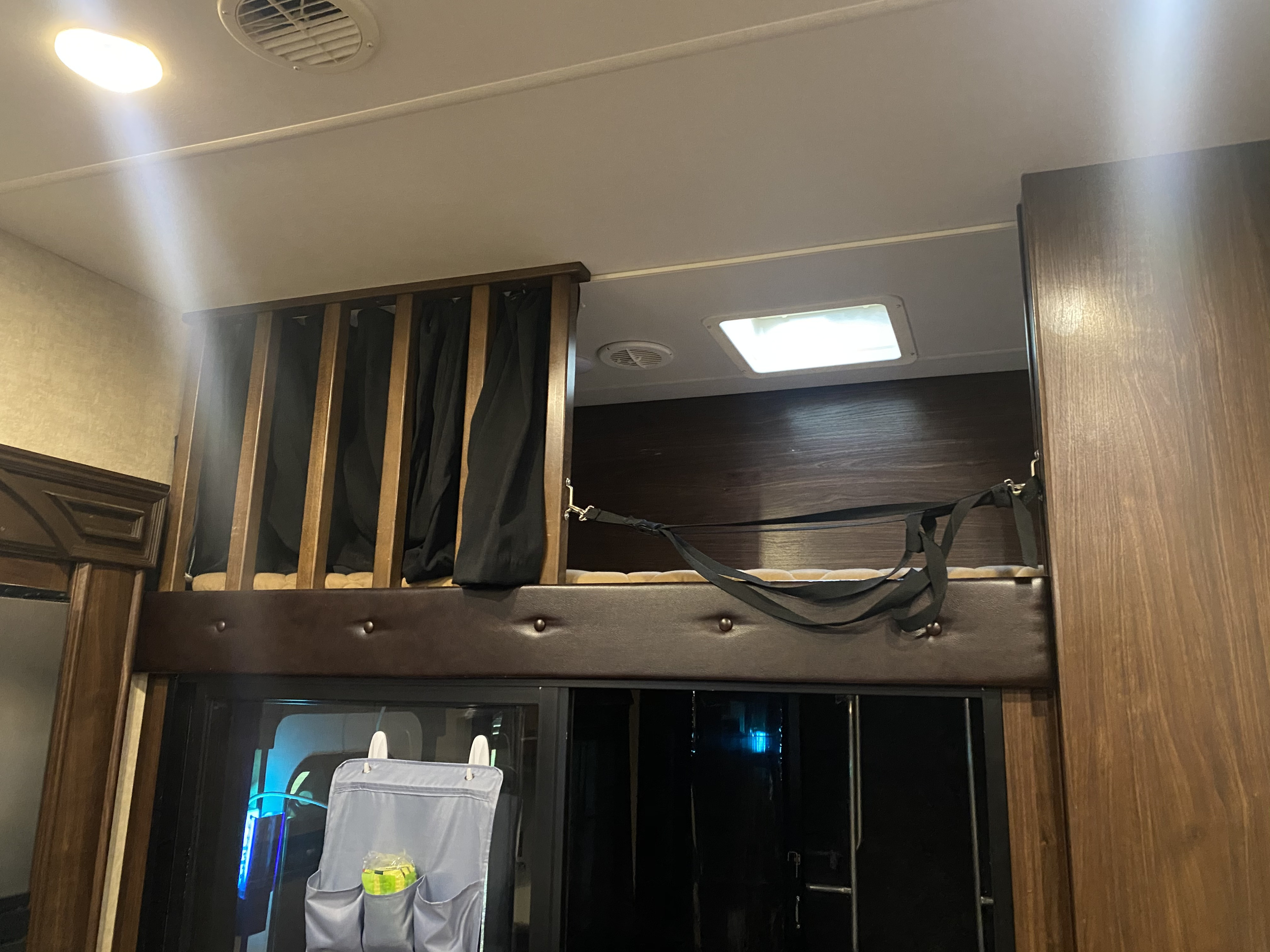 RV rental interior: A stacked bunk bed setup with wooden railings, black privacy curtains, and a safety strap.. Heartland Cyclone 2015