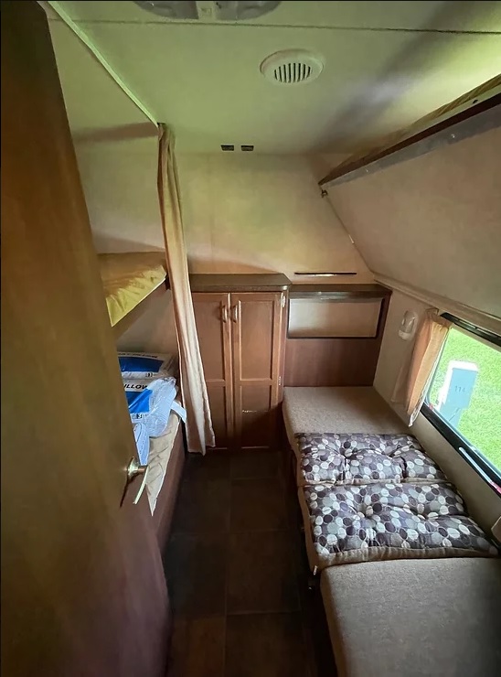 Inside an RV rental: bunk beds with privacy curtain, central storage cabinet, and a flexible seating area by the window.. Crossroads RV Slingshot 2012