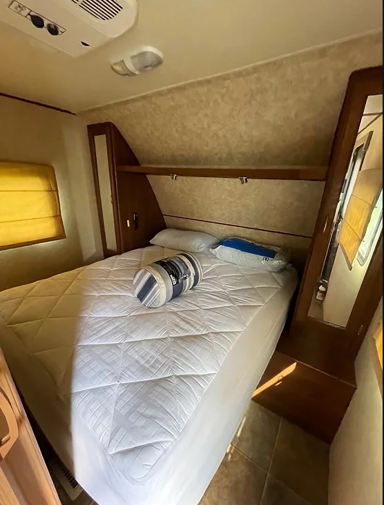 RV rental bedroom interior: a white quilted bed, overhead shelving, and AC unit provide comfort in this compact space.. Crossroads RV Slingshot 2012