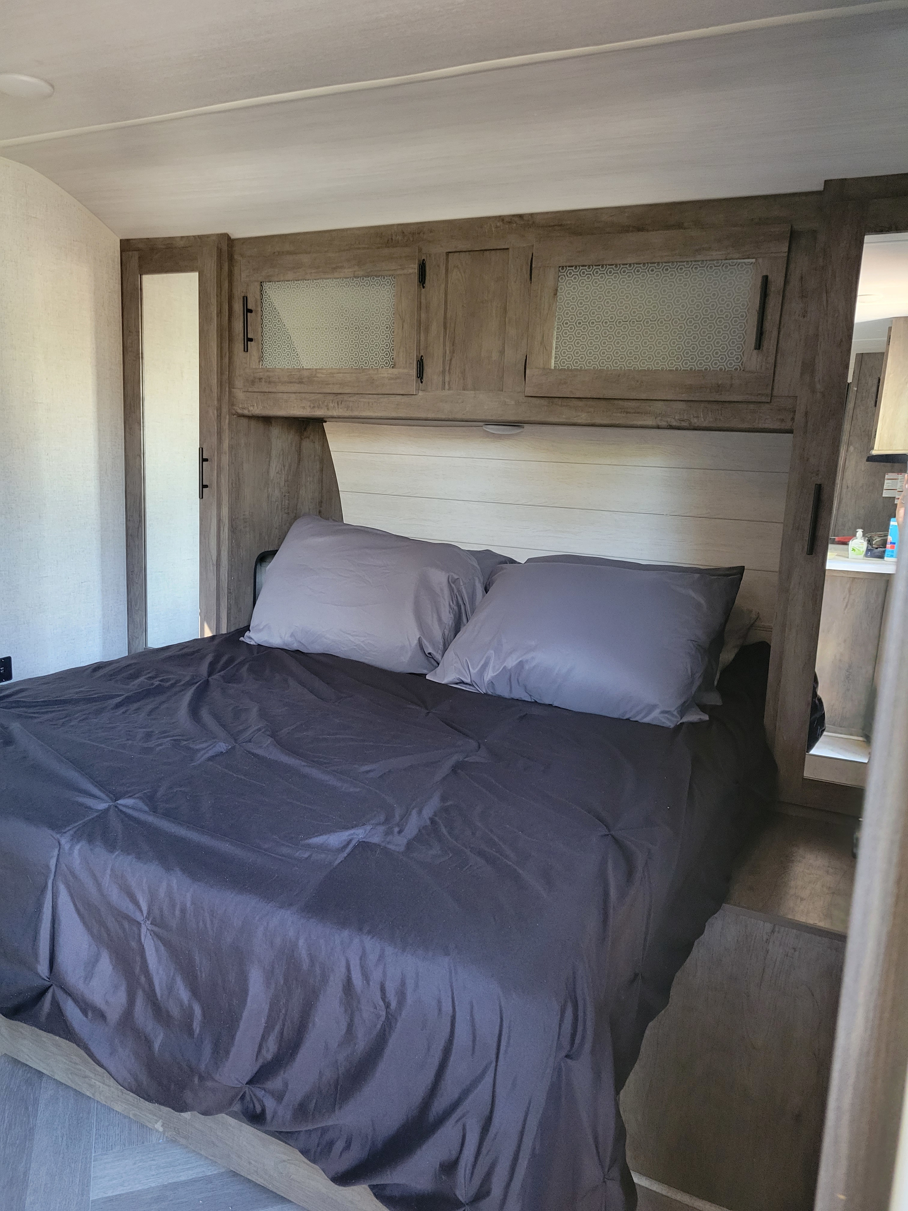 Modern RV rental bedroom featuring a comfy bed with dark linens, overhead cabinets, and built-in wardrobes for organized living.. Salem Forester 32bhds 2020