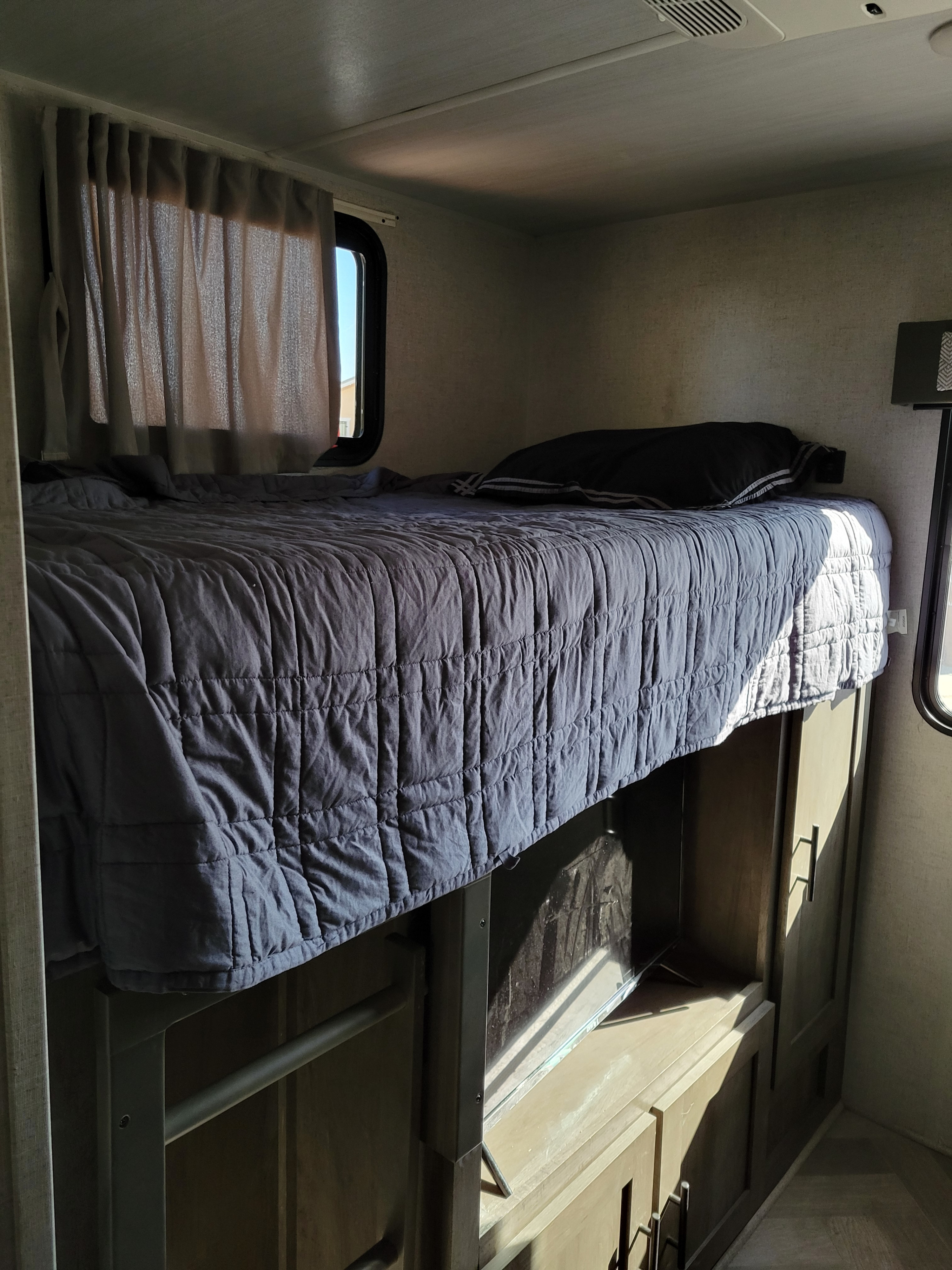 Cozy RV rental bunk bed with a gray comforter, black pillow, and a TV with storage cabinet below.. Salem Forester 32bhds 2020