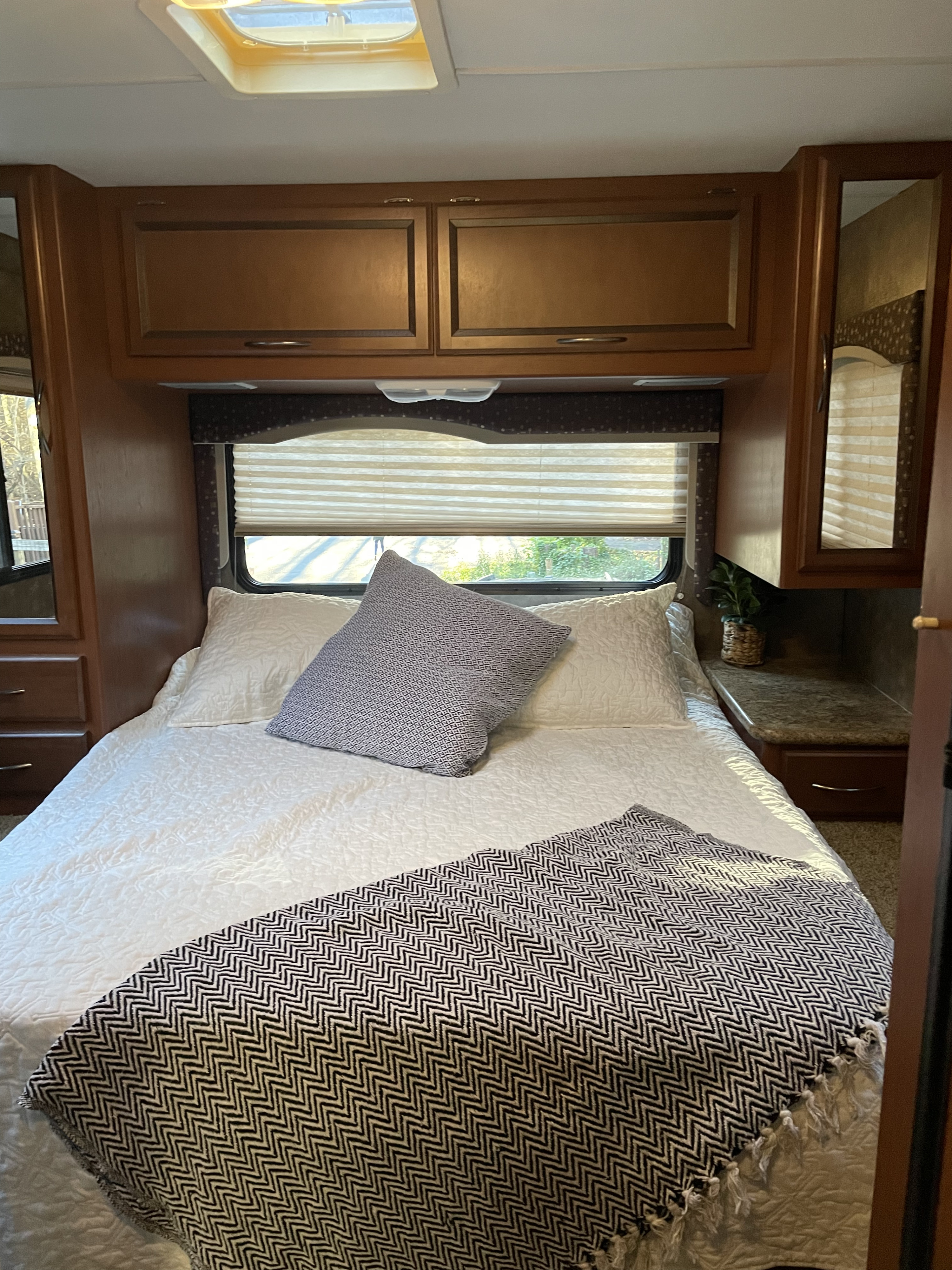 Cozy RV rental bedroom featuring a comfortable bed with white bedding, overhead cabinets, and a window with blinds.. Thor Freedom Elite 2013
