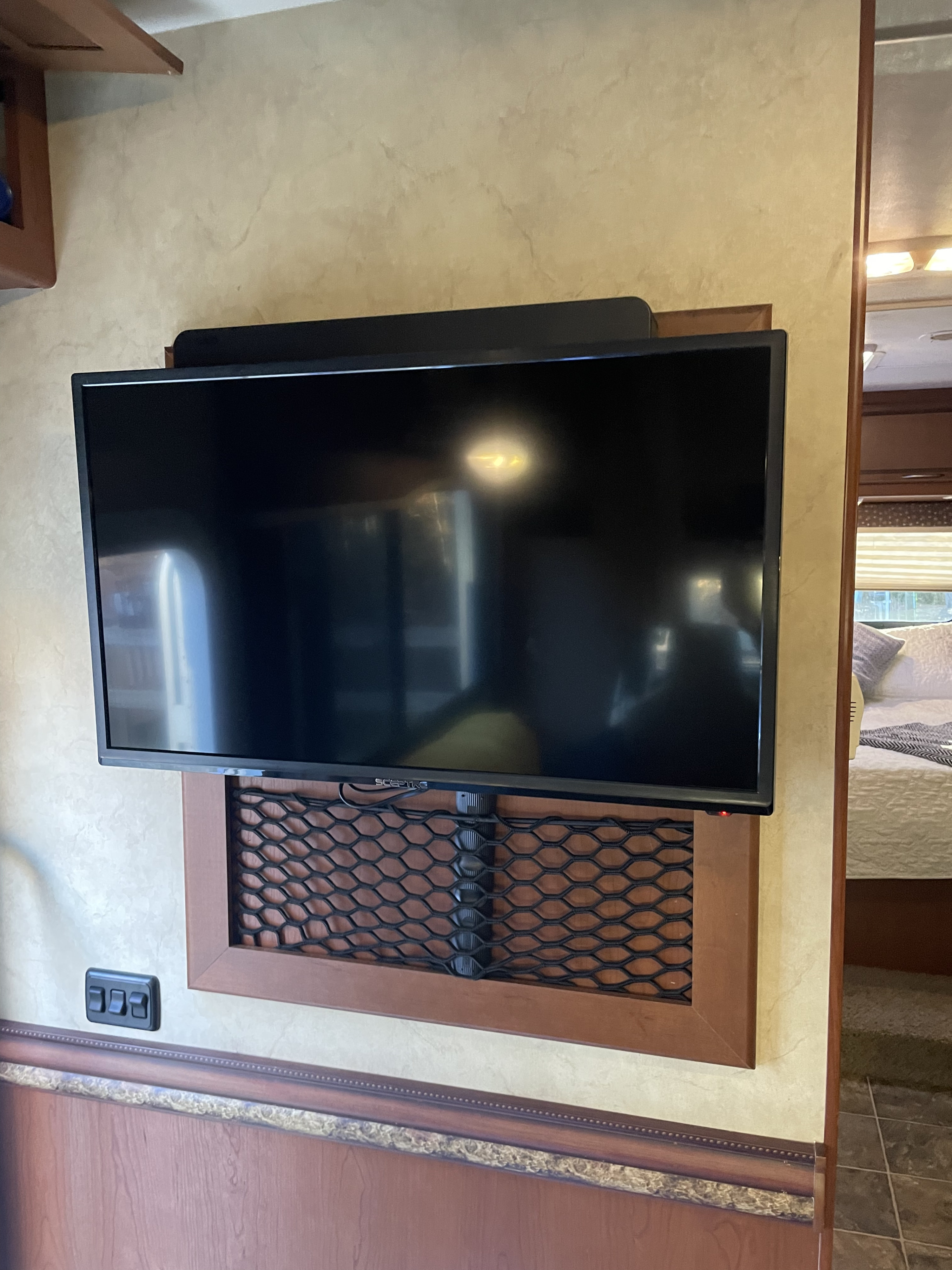Cozy RV rental interior with a wall-mounted TV, practical storage net, and light switches, peeking into the bedroom.. Thor Freedom Elite 2013