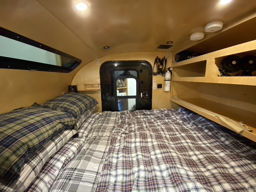 Cozy RV rental interior with a plaid bed filling the space, window, and storage shelves. Perfect for compact adventures.. Teardrop Camping Company Teardrop 2021