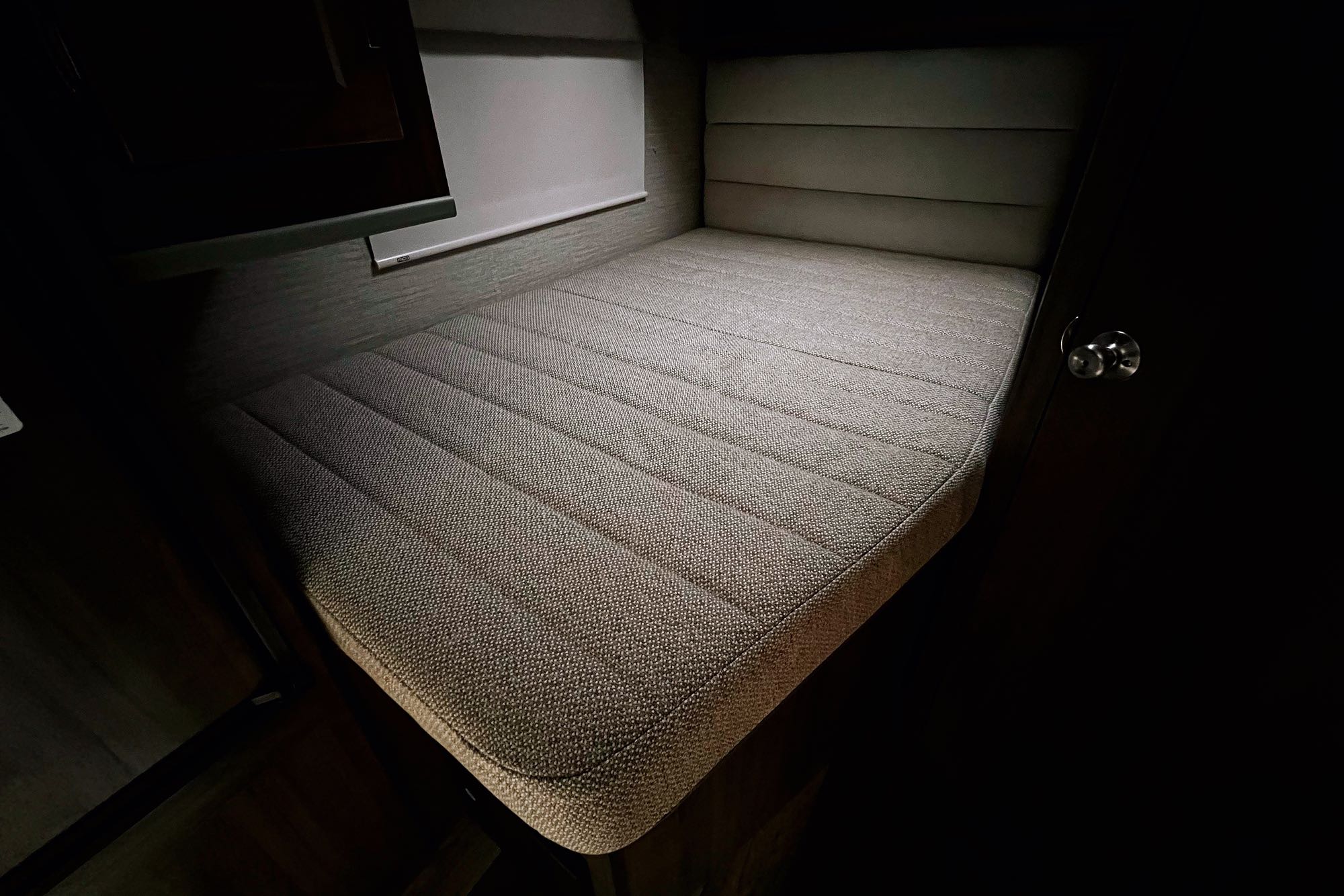 Cozy rv rental bed: textured mattress, padded headboard, and window in a compact sleeping area.. Winnebago Spirit 2020