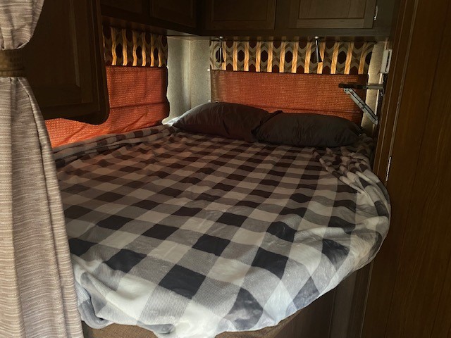 An inviting RV rental bedroom with a comfy bed, plaid blanket, and practical wall shelf.. Coachmen Leprechan 2017