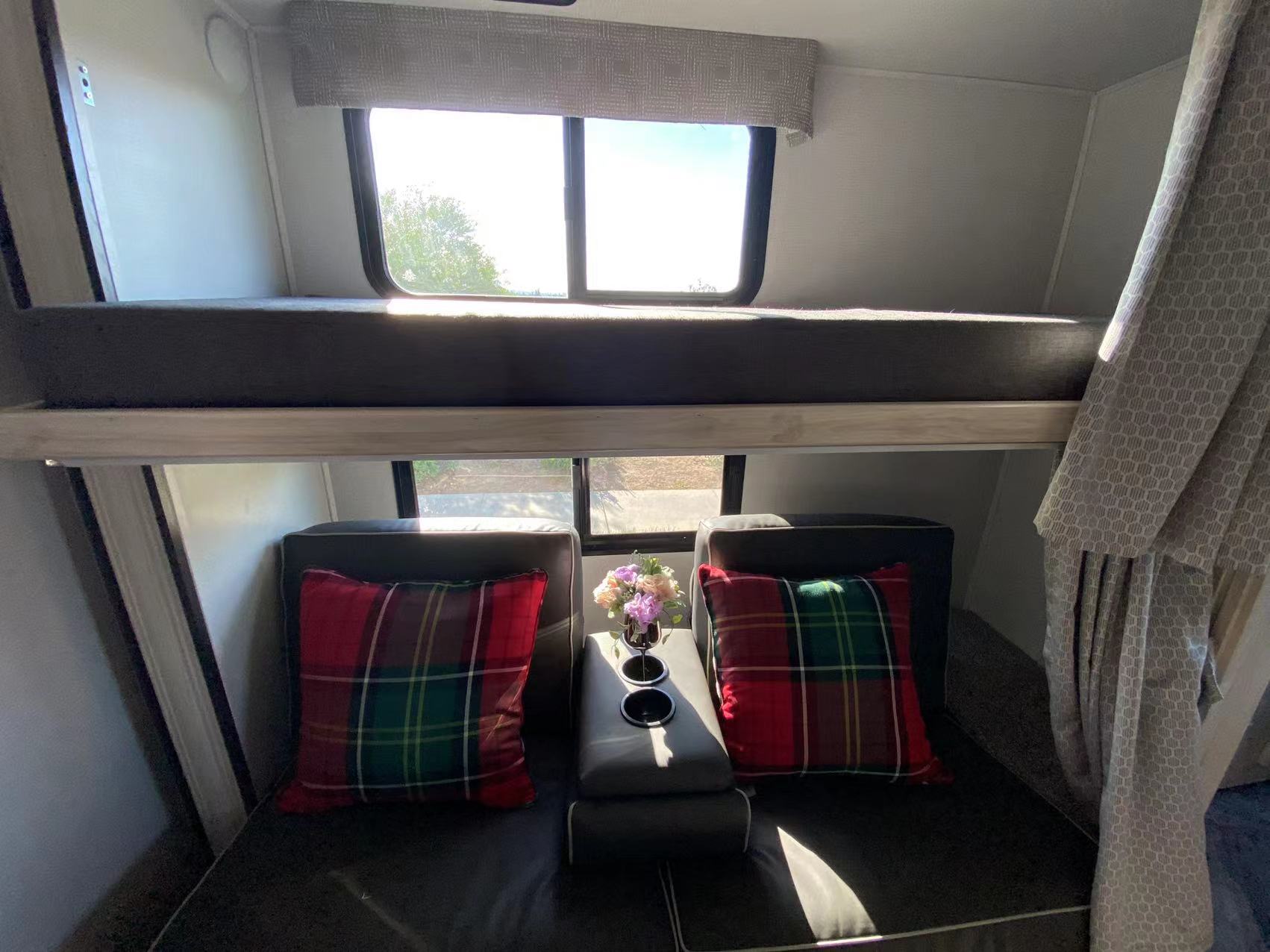 Inside an RV rental: a top bunk, lower seating with plaid pillows, console, and bright windows reveal the outdoors.. Forest River Sunseeker 2022