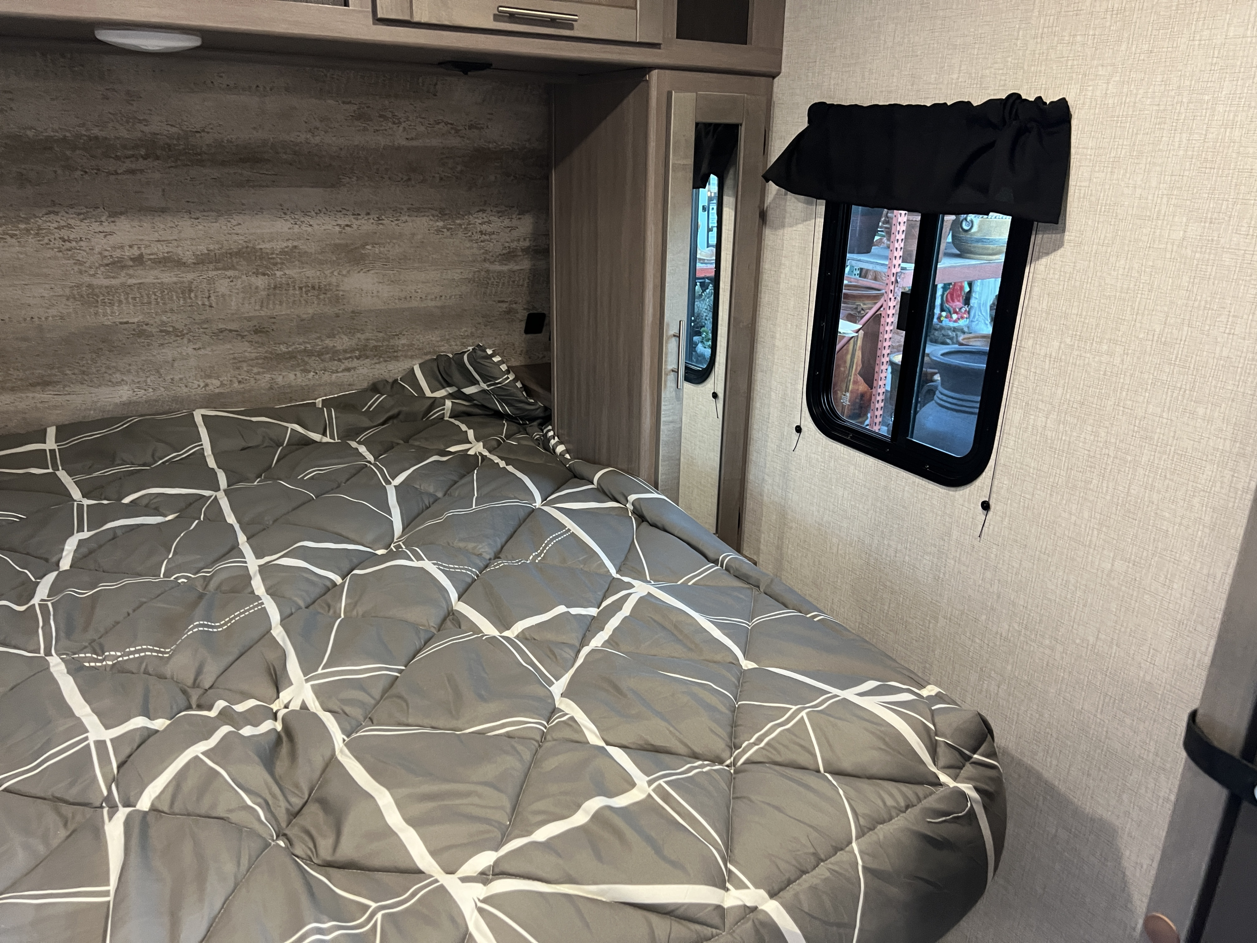 Cozy RV rental bedroom featuring a grey patterned comforter, a small window, and convenient overhead storage.. Crossroads Sunset Trail 2021