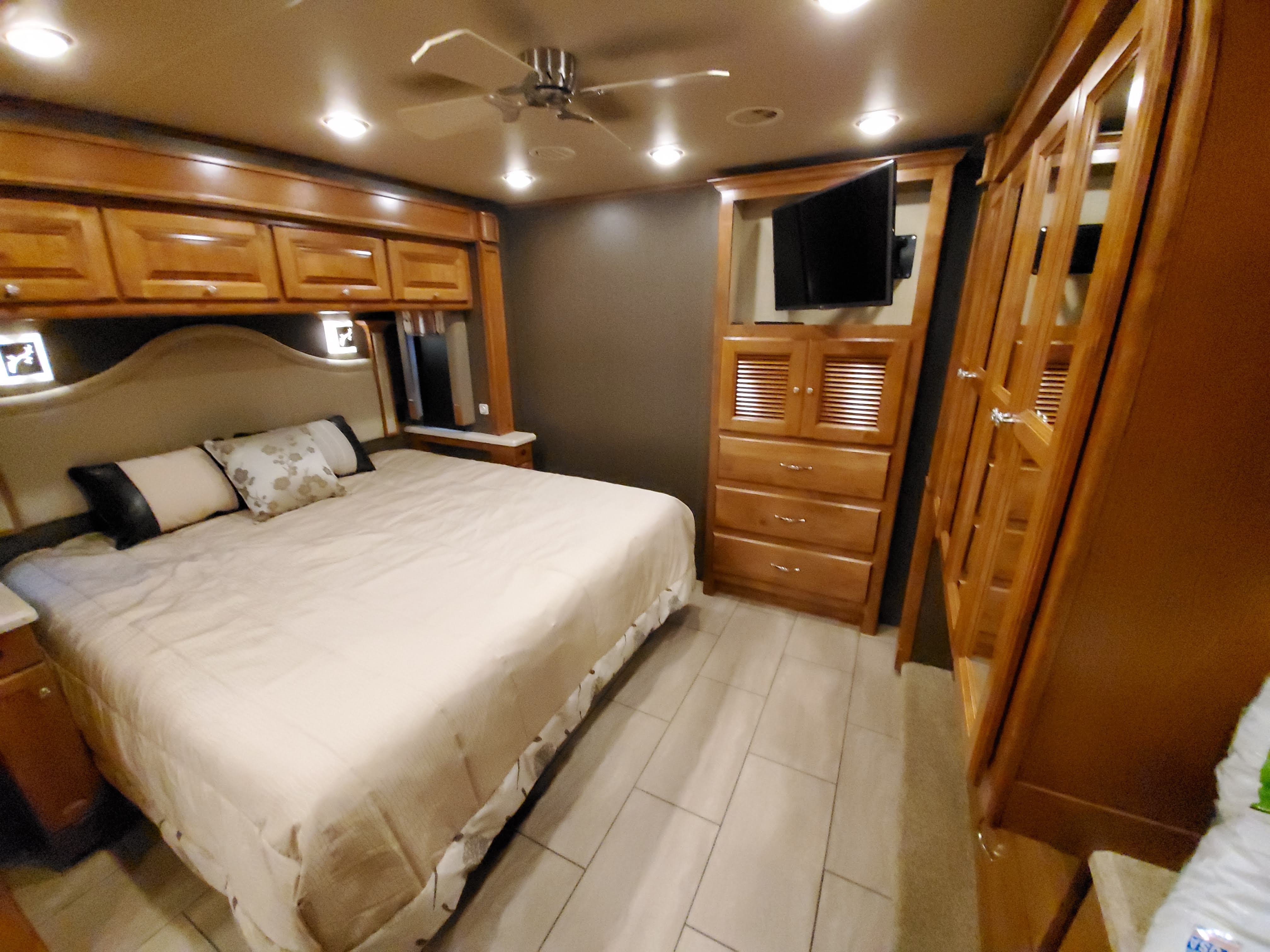 This inviting RV rental bedroom features a comfy queen bed, ample wood storage, TV, and ceiling fan for a cozy journey.. Tiffin Motorhomes Allegro Open Road 2016