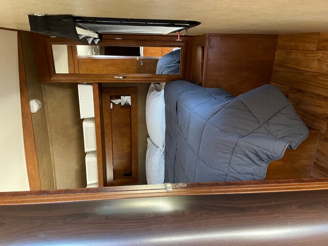 Cozy RV rental bedroom featuring a made bed, wood paneling, mirrored cabinet, and white storage baskets.. Forest River Vibe Extreme Lite 2016