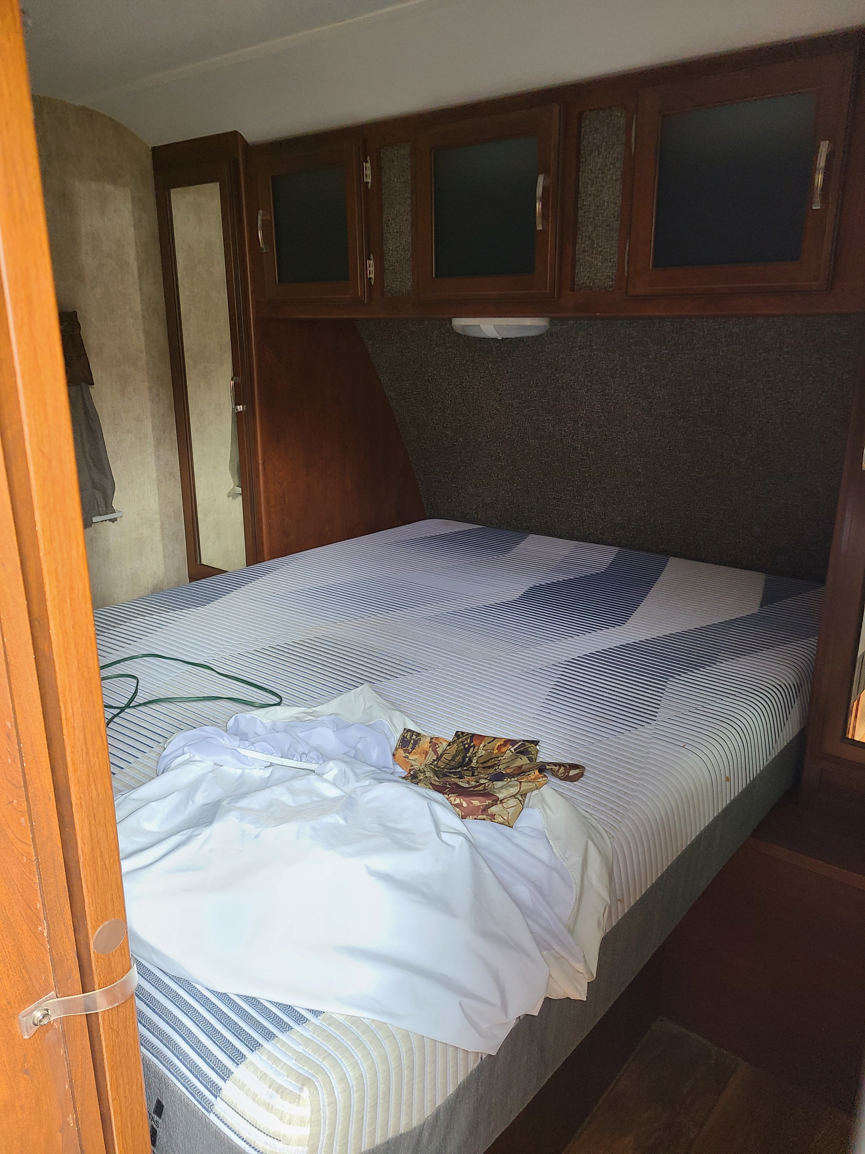 RV rental bedroom with a bed featuring a modern striped mattress, dark wood overhead cabinets, and a tall mirror.. Keystone Passport Ultra-lite Grand Touring 2016