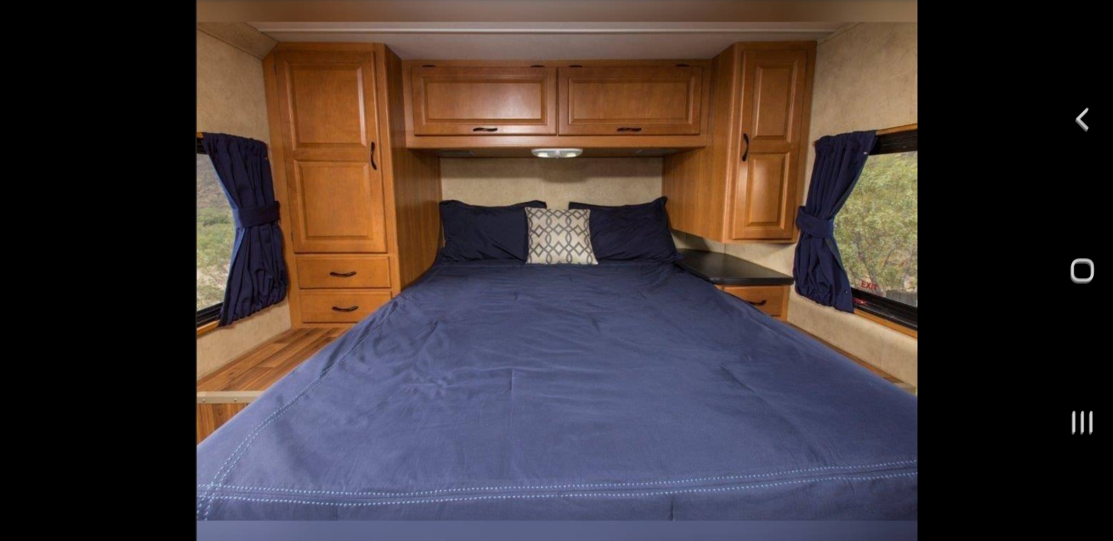 Compact RV rental bedroom featuring a comfy blue bed, built-in wooden cabinets, and side windows with drapes.. Four Winds Majestic 2011