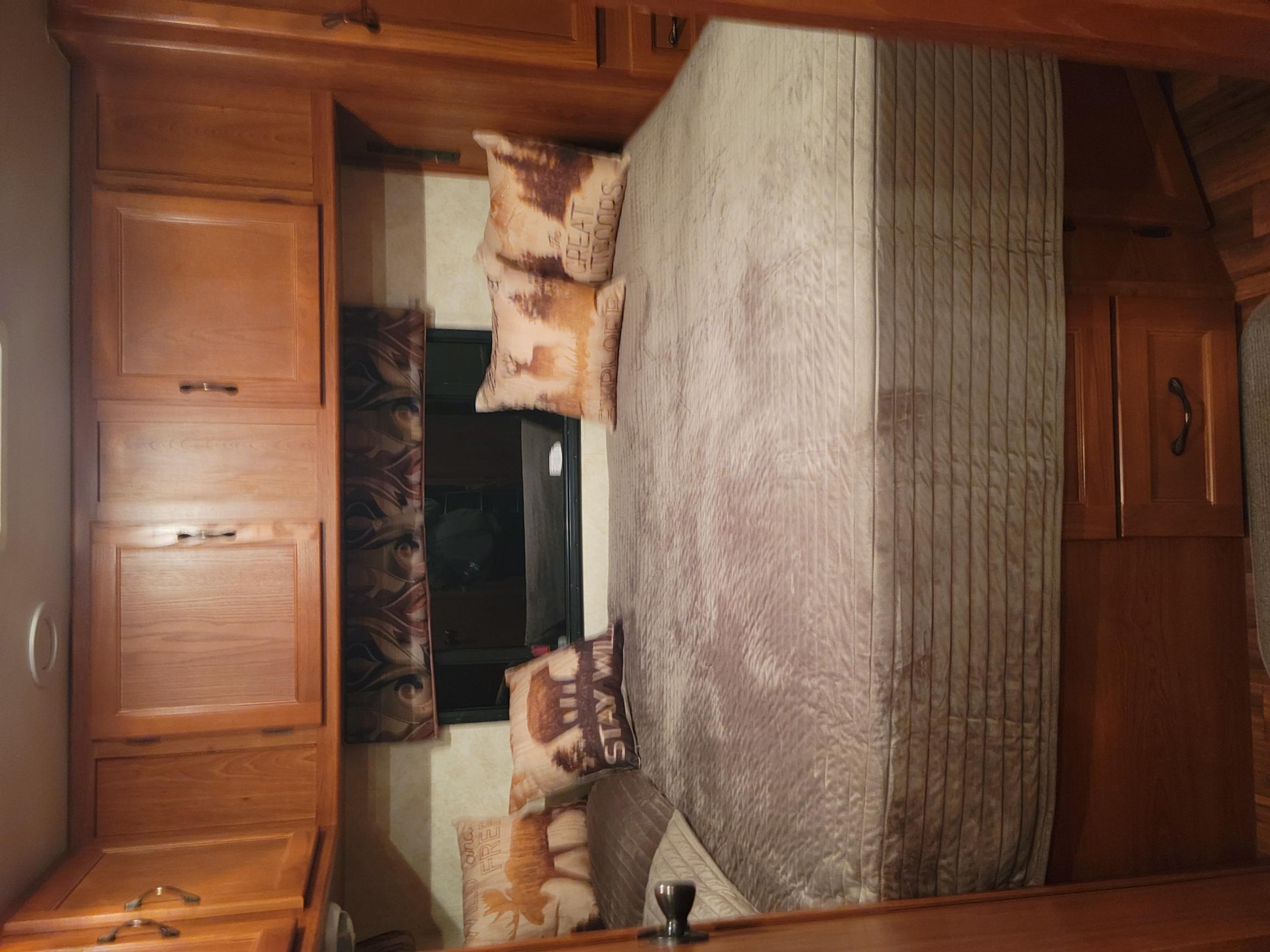 Step into comfort! This RV rental bedroom features warm wood cabinets, a comfy bed, and nature-themed pillows.. Coachmen Freelander 2011