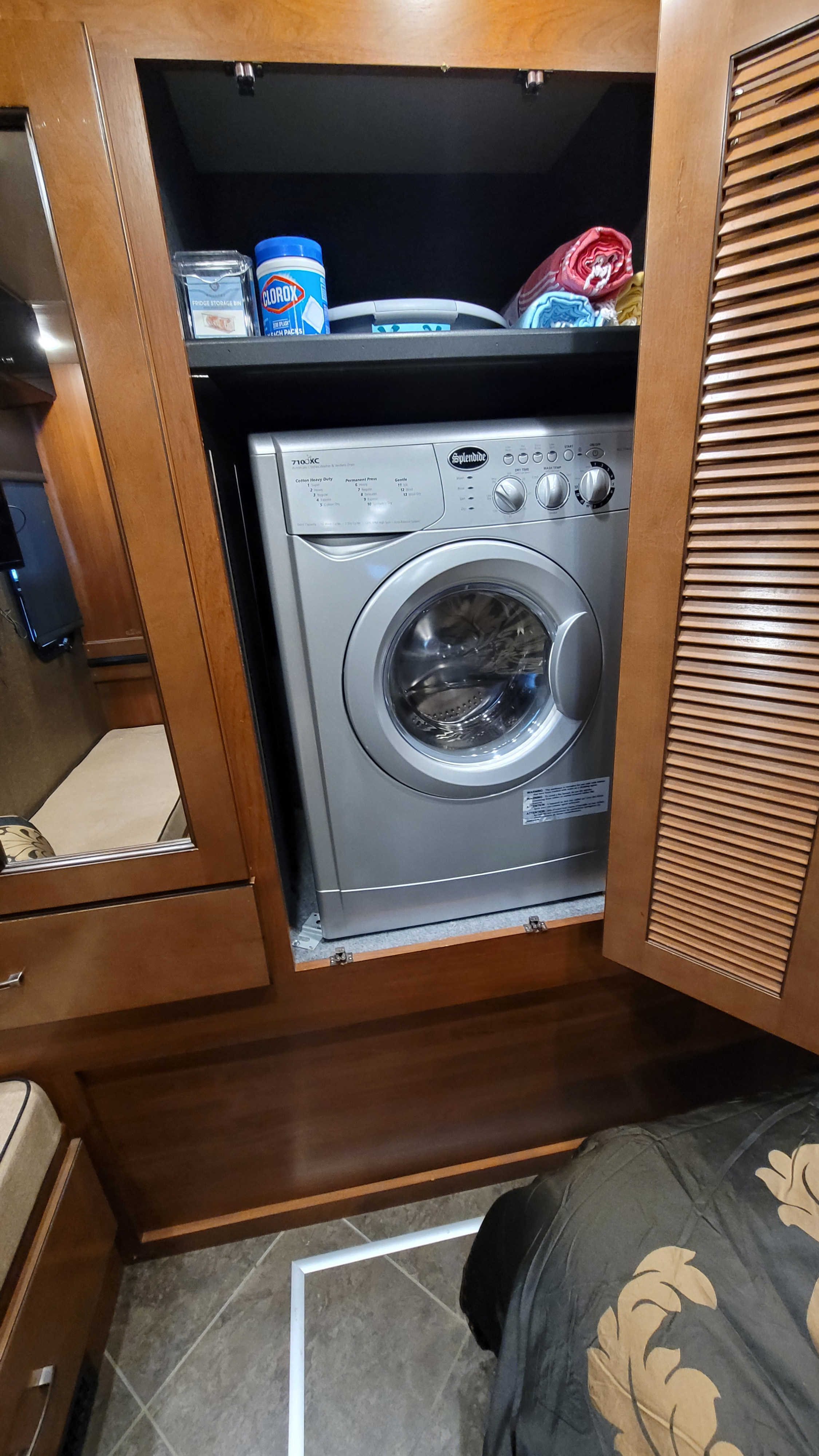 Compact Splendide washer/dryer unit inside a cabinet of an RV rental. Cleaning supplies are on the shelf above.. Fleetwood 35E 2015